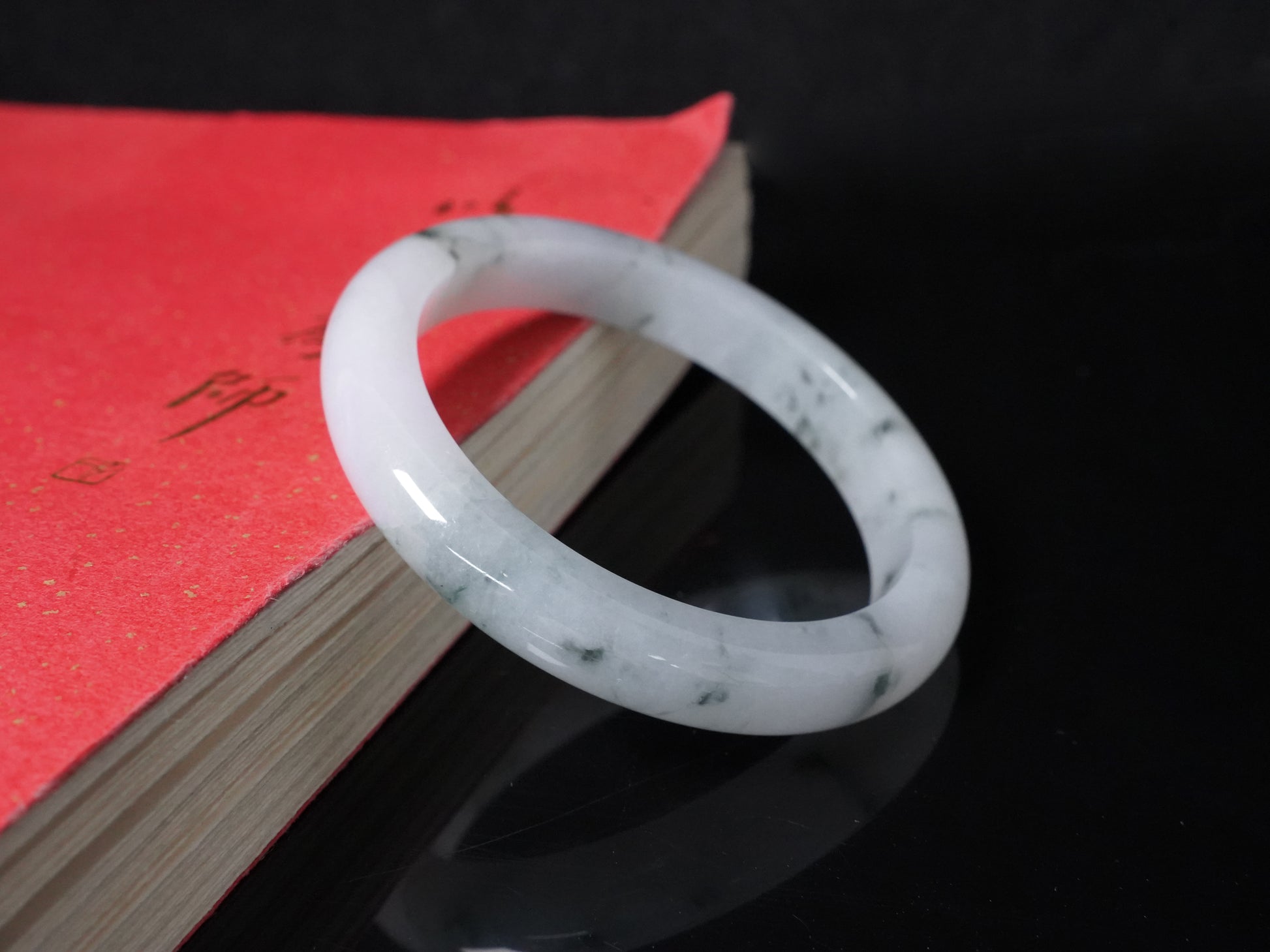 This jadeite bangle features a milky base adorned with delicate ink-wash veining.