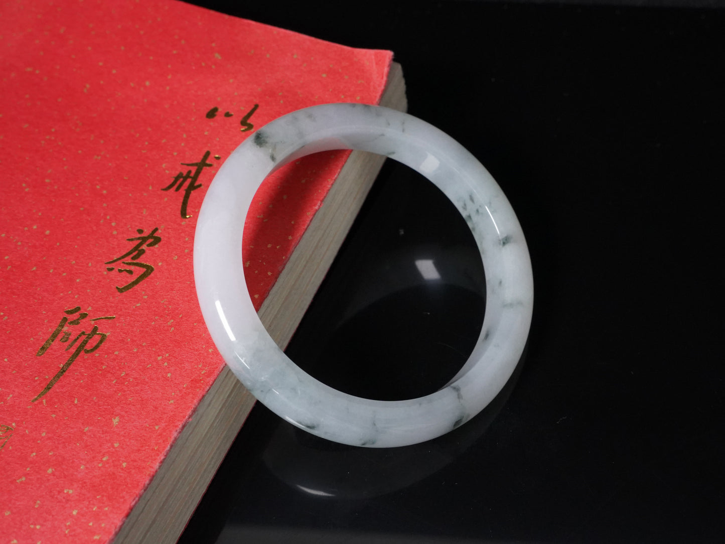 This jadeite bangle features a milky base adorned with delicate ink-wash veining.