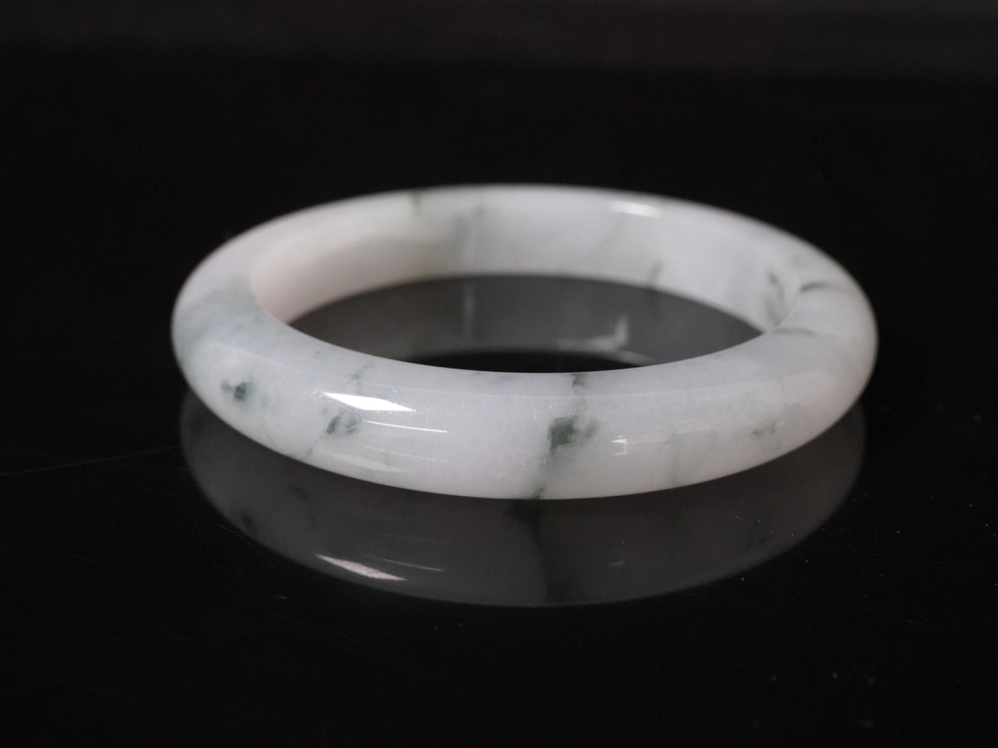 This jadeite bangle features a milky base adorned with delicate ink-wash veining.