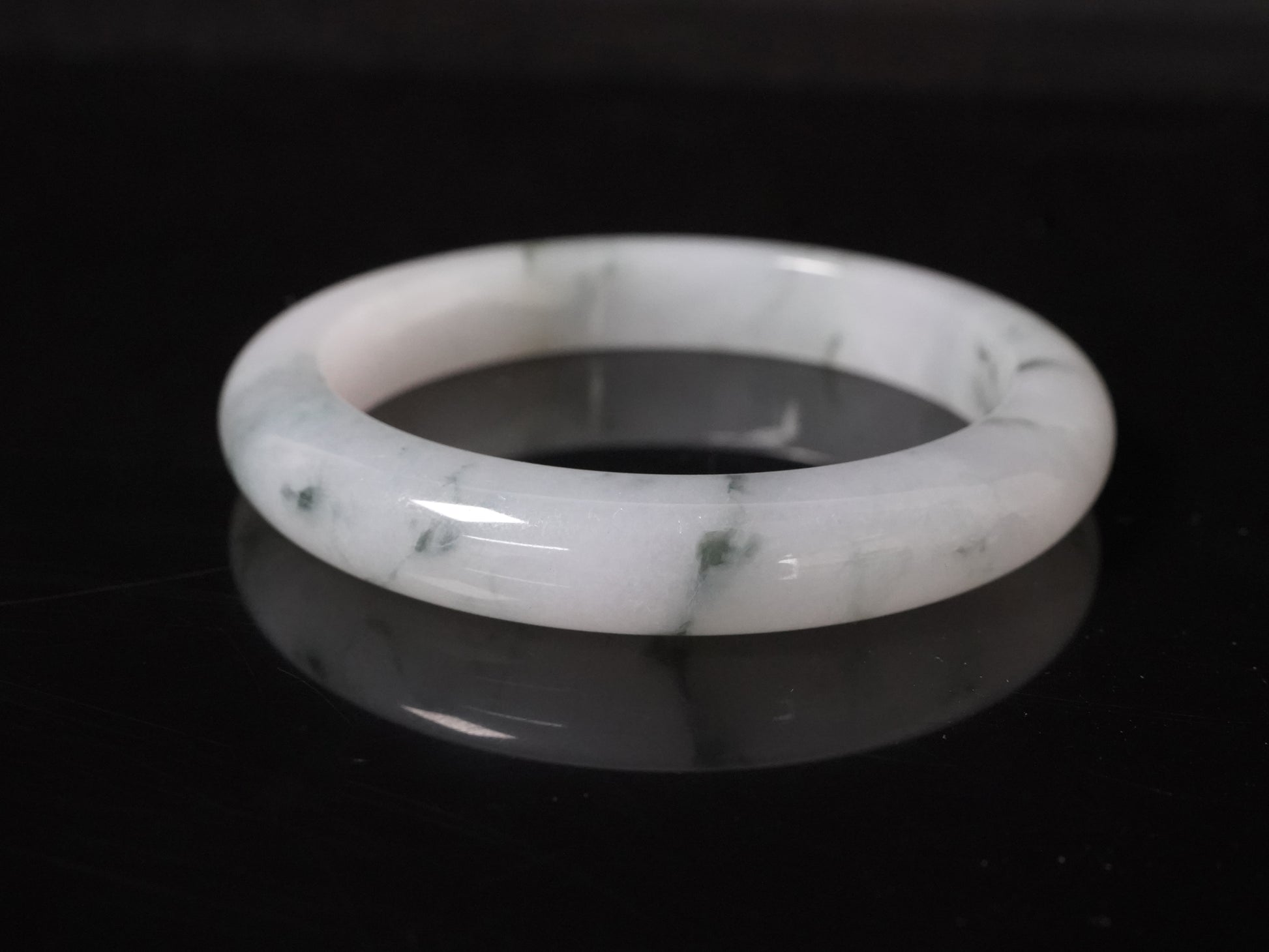 This jadeite bangle features a milky base adorned with delicate ink-wash veining.