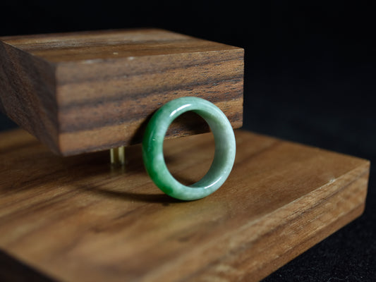 Green jade ring on a wooden stand with a dark background