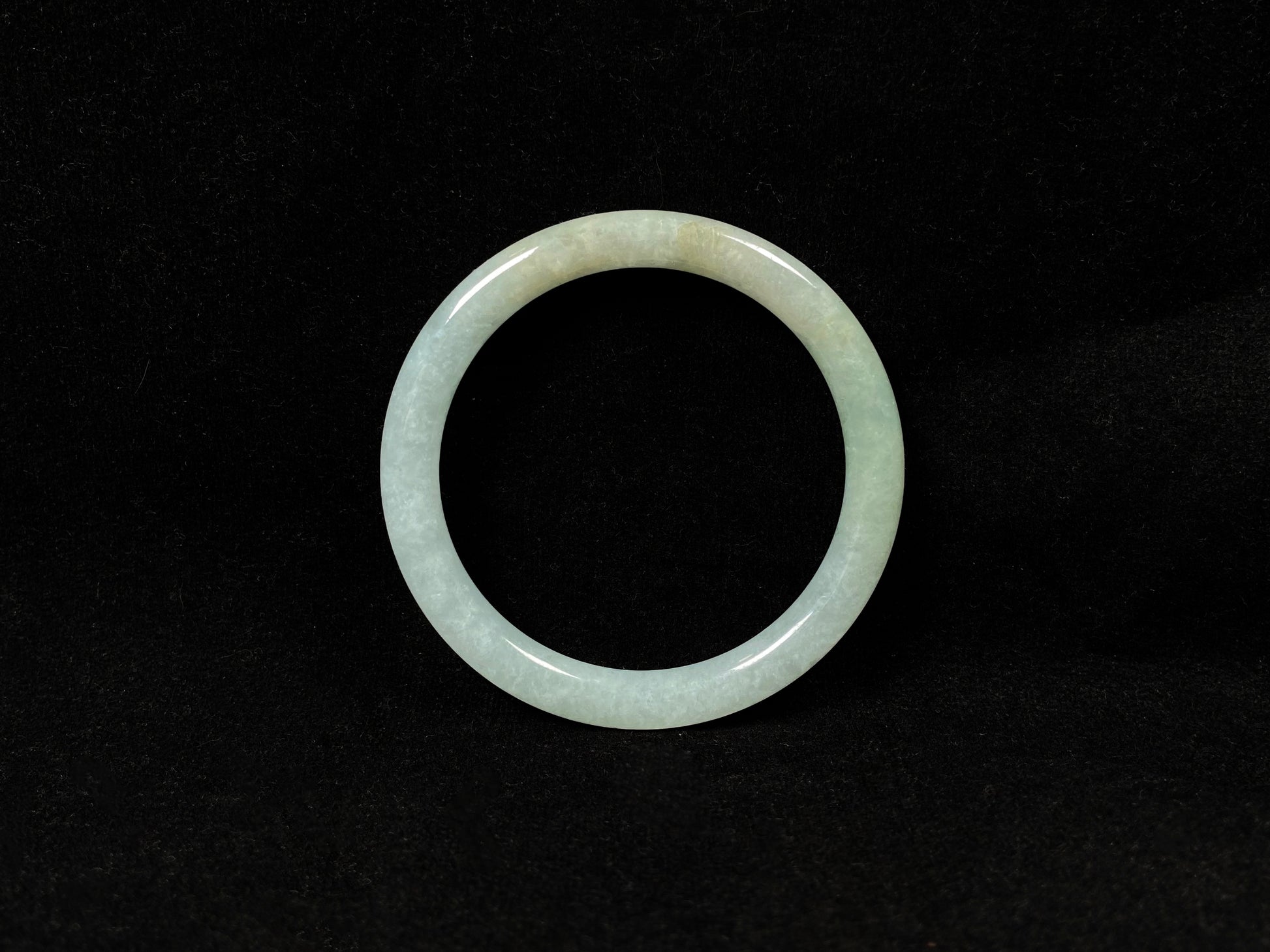 This jadeite bangle has a soft pale cyan base with cream undertones and faint gold streaks.