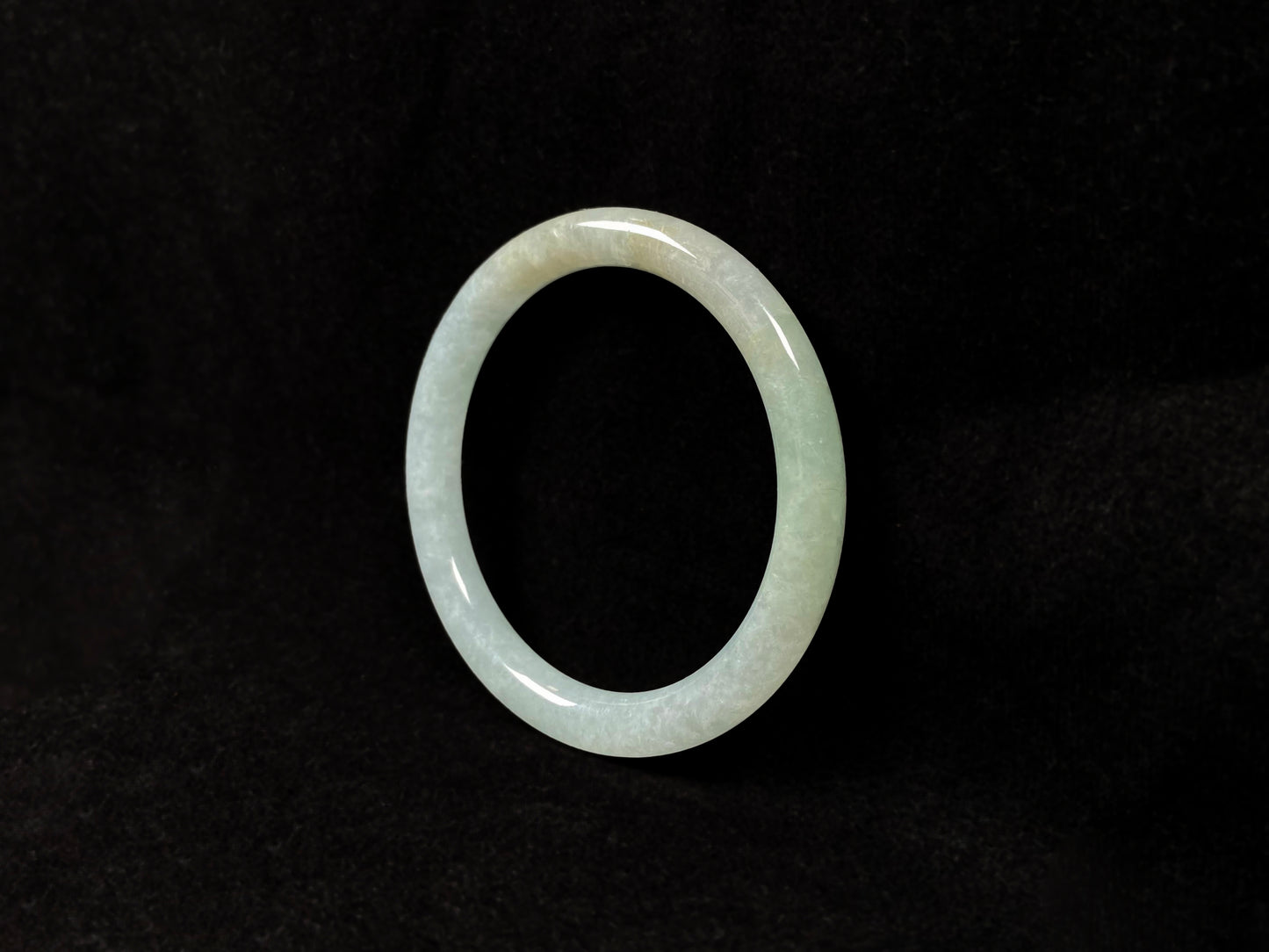 This jadeite bangle has a soft pale cyan base with cream undertones and faint gold streaks.