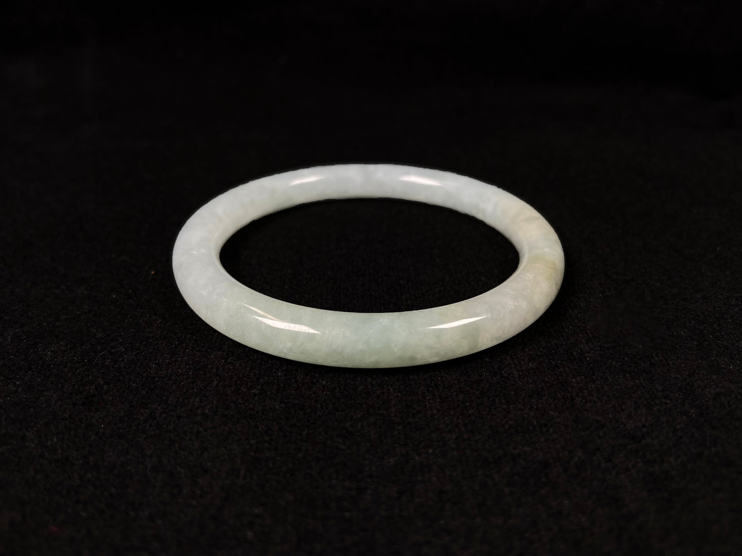 This jadeite bangle has a soft pale cyan base with cream undertones and faint gold streaks.