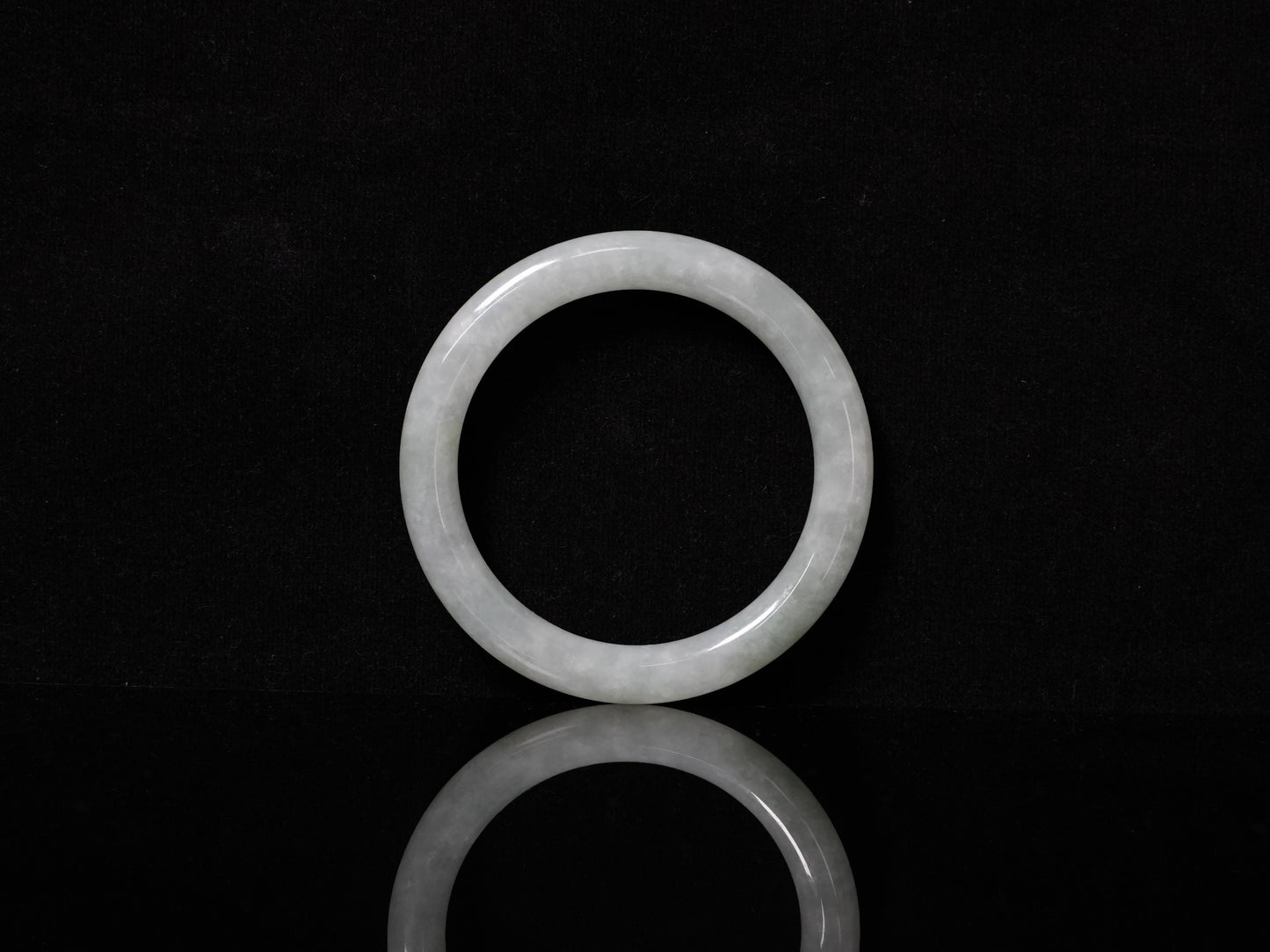 This Burmese jadeite bangle features a soft pale ash-white hue, with a smooth, luminous and subtly frosted finish.