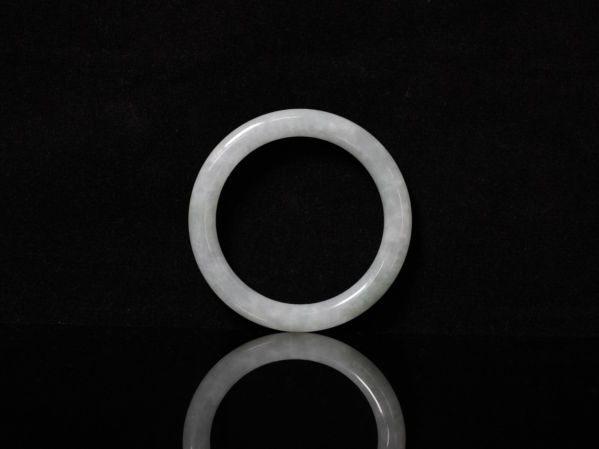 This Burmese jadeite bangle features a soft pale ash-white hue, with a smooth, luminous and subtly frosted finish.