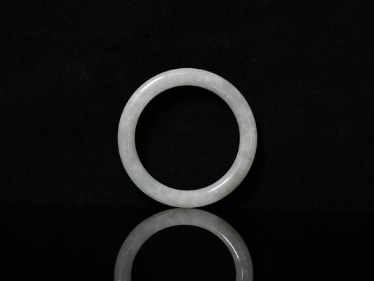 This Burmese jadeite bangle features a soft pale ash-white hue, with a smooth, luminous and subtly frosted finish.