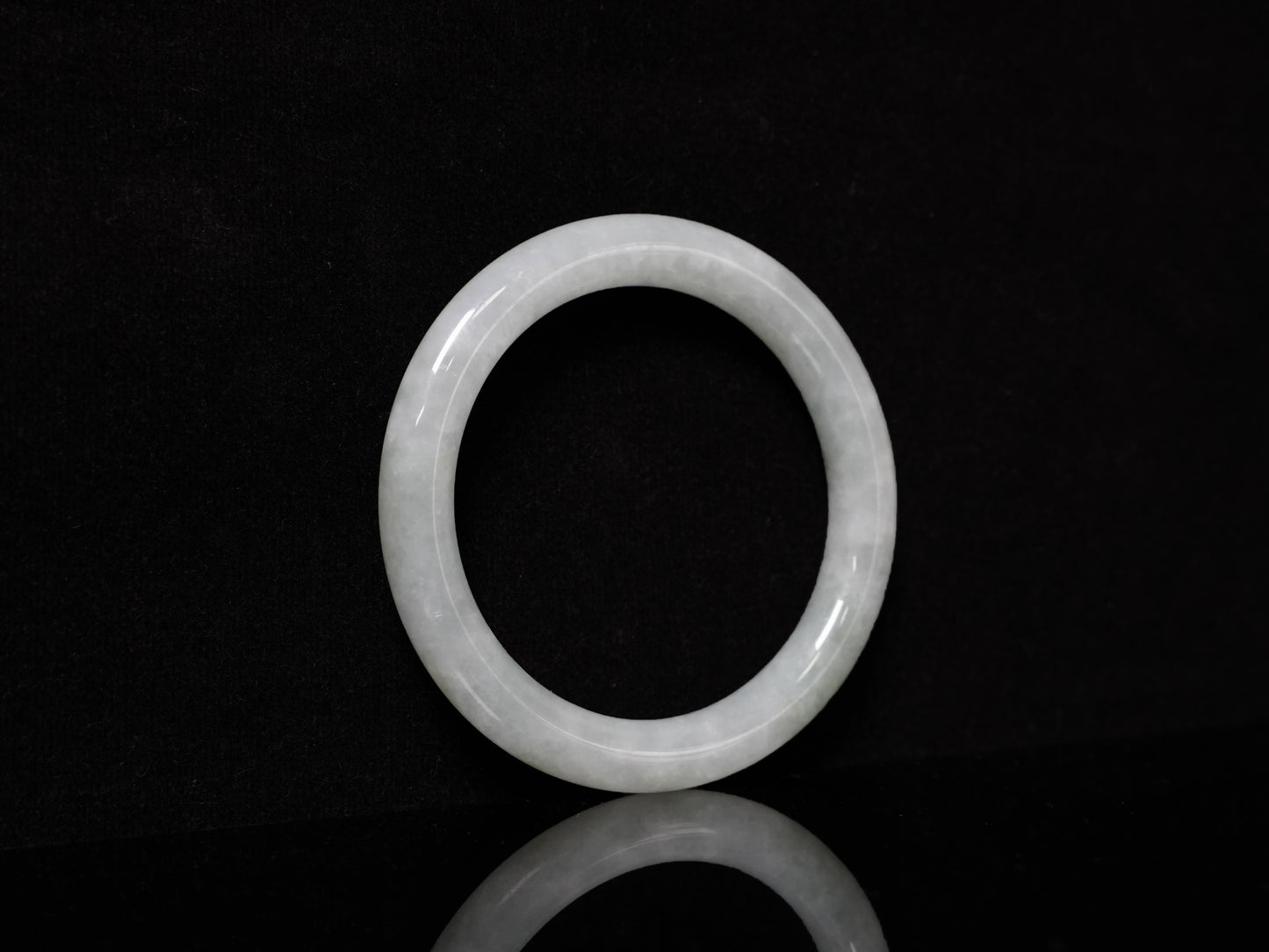This Burmese jadeite bangle features a soft pale ash-white hue, with a smooth, luminous and subtly frosted finish.