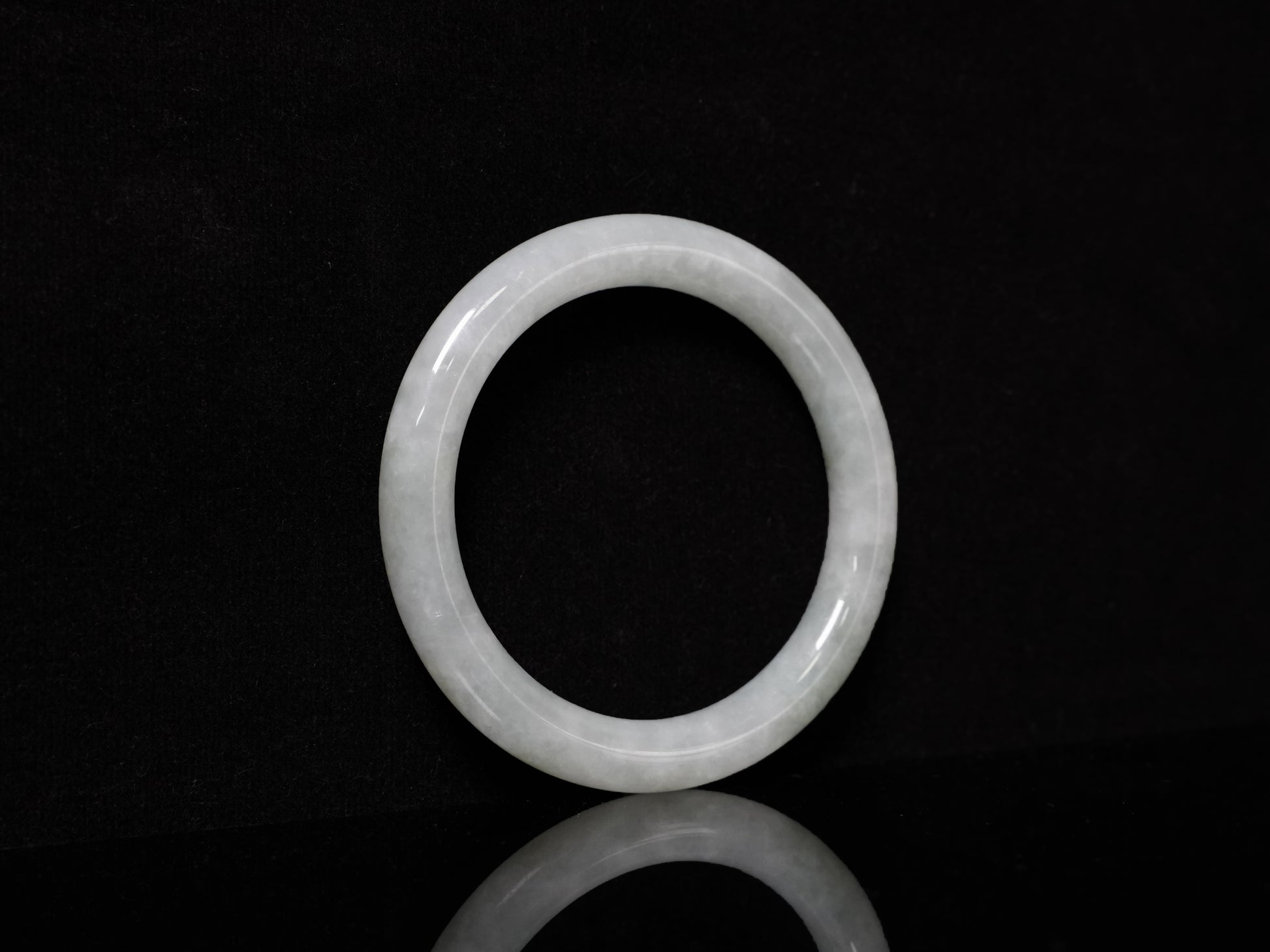 This Burmese jadeite bangle features a soft pale ash-white hue, with a smooth, luminous and subtly frosted finish.