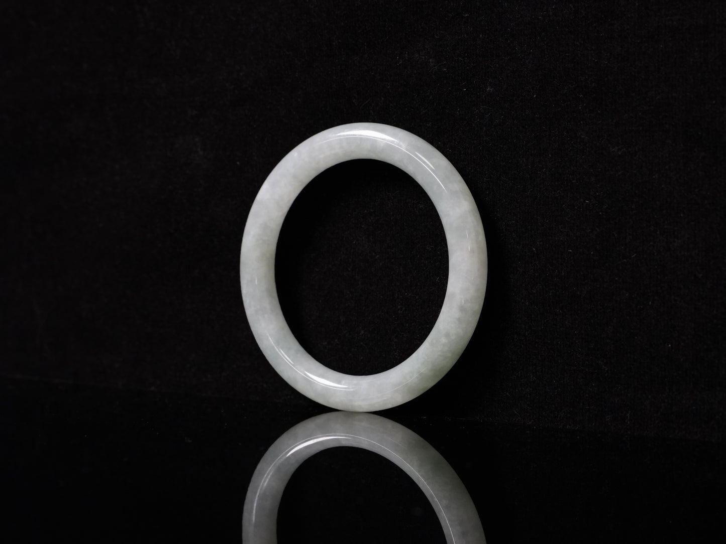 This Burmese jadeite bangle features a soft pale ash-white hue, with a smooth, luminous and subtly frosted finish.