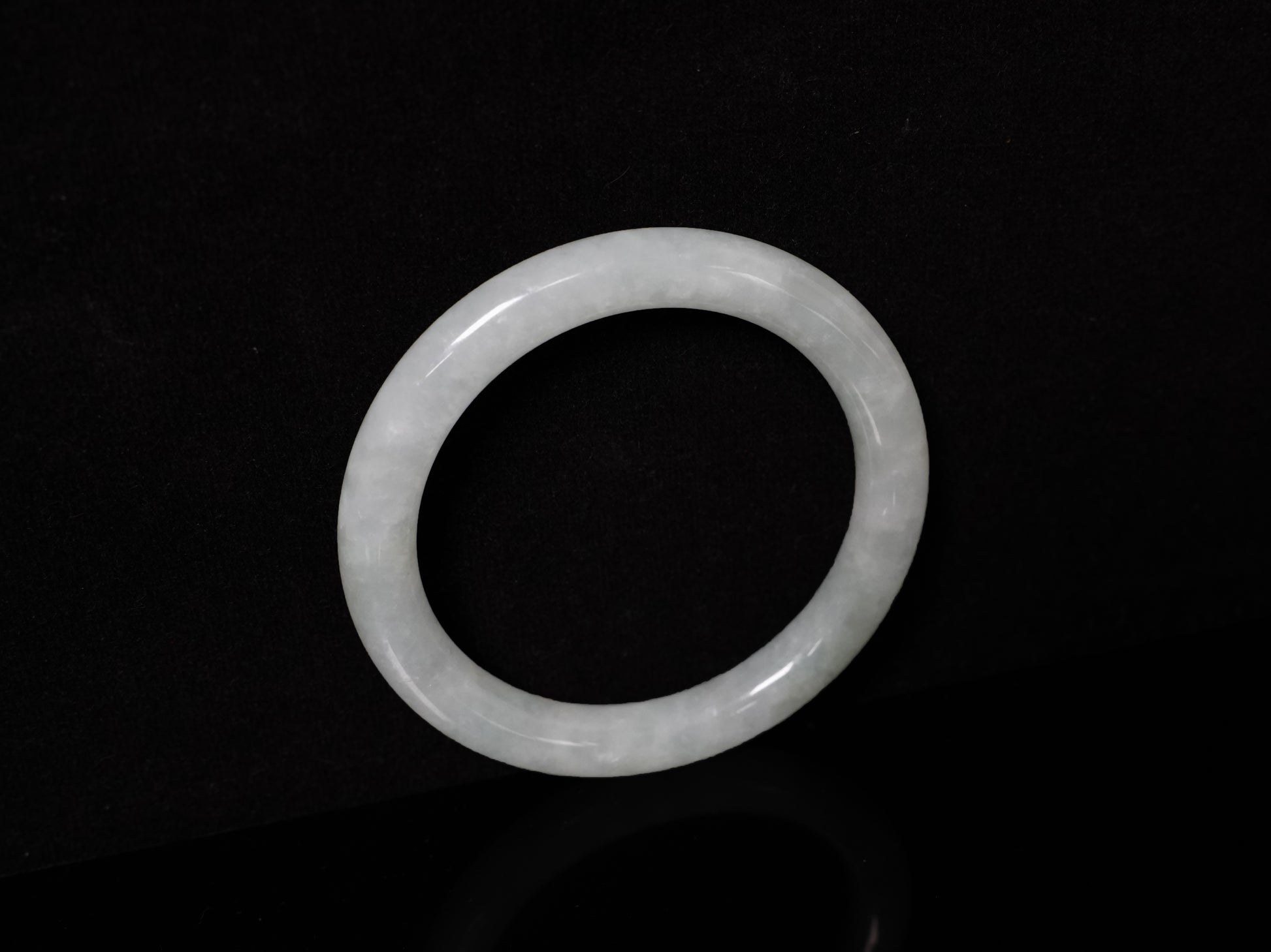 This Burmese jadeite bangle features a soft pale ash-white hue, with a smooth, luminous and subtly frosted finish.