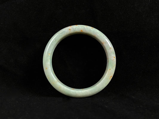 A white and green jade bangle with speckled gold inclusions