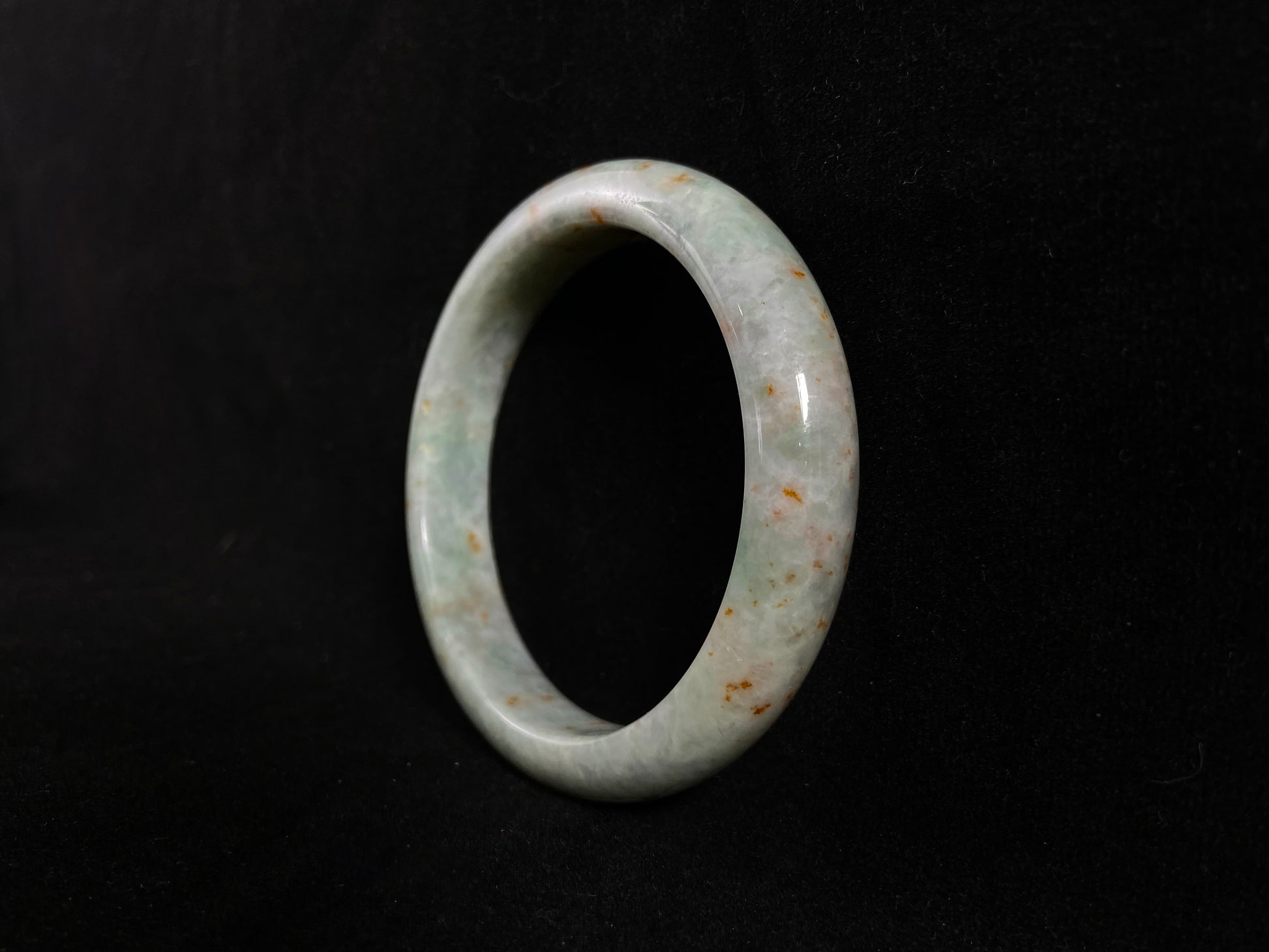 A white and green jade bangle with speckled gold inclusions