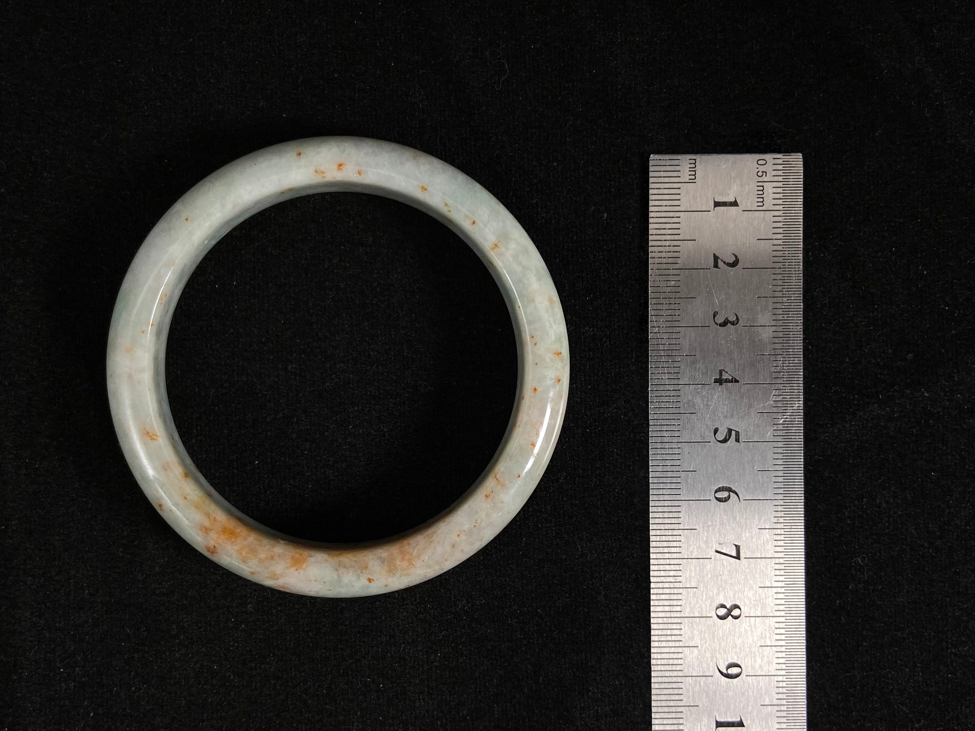 A white and green jade bangle with speckled gold inclusions