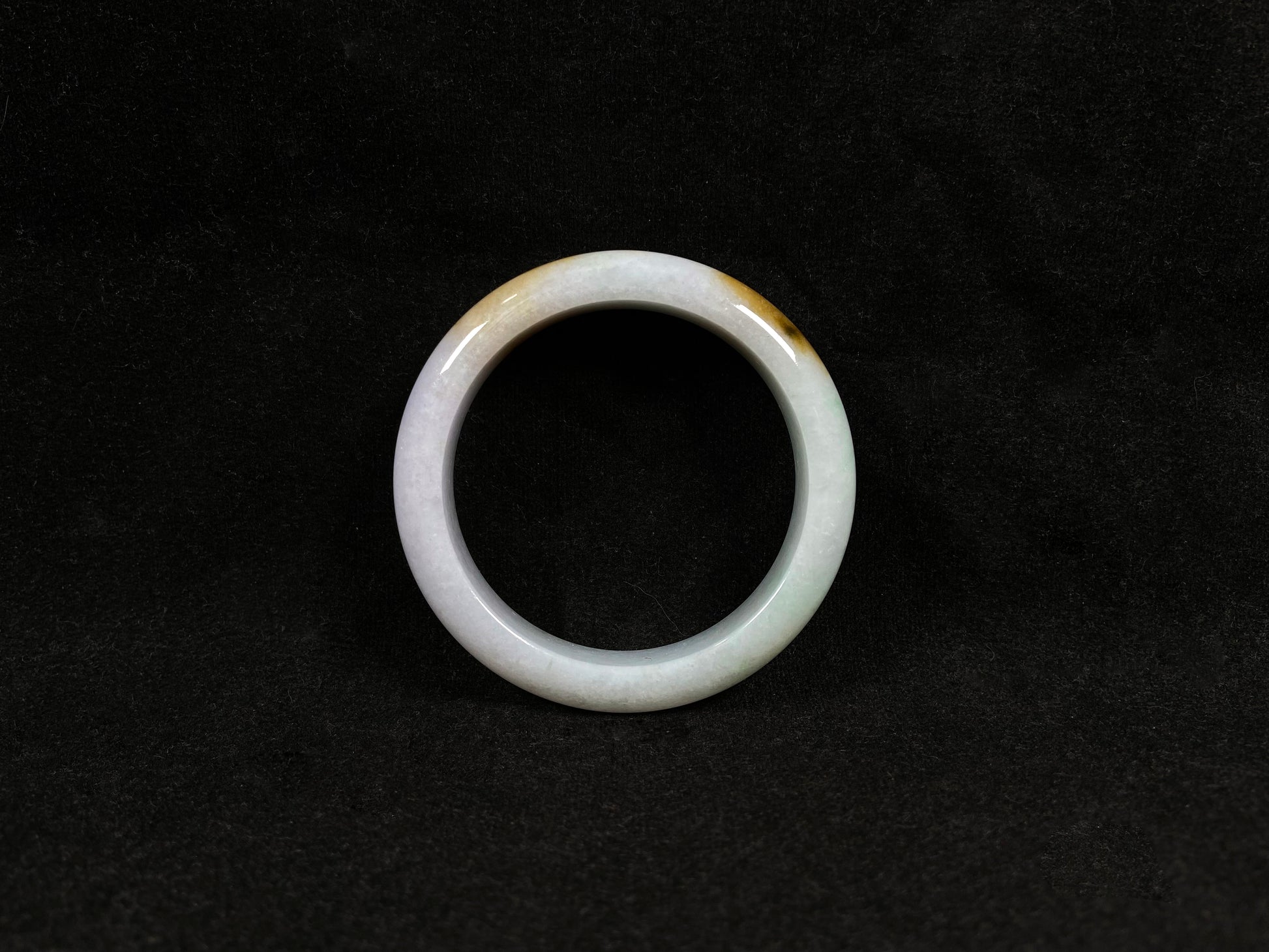 A  white jadeite bangle featuring purple, gold, and light green tones.
