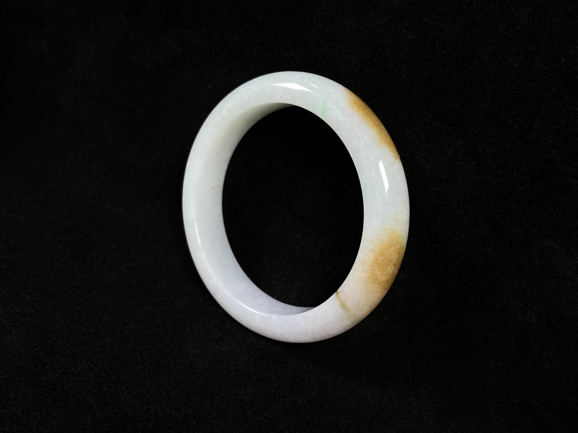 A  white jadeite bangle featuring purple, gold, and light green tones.