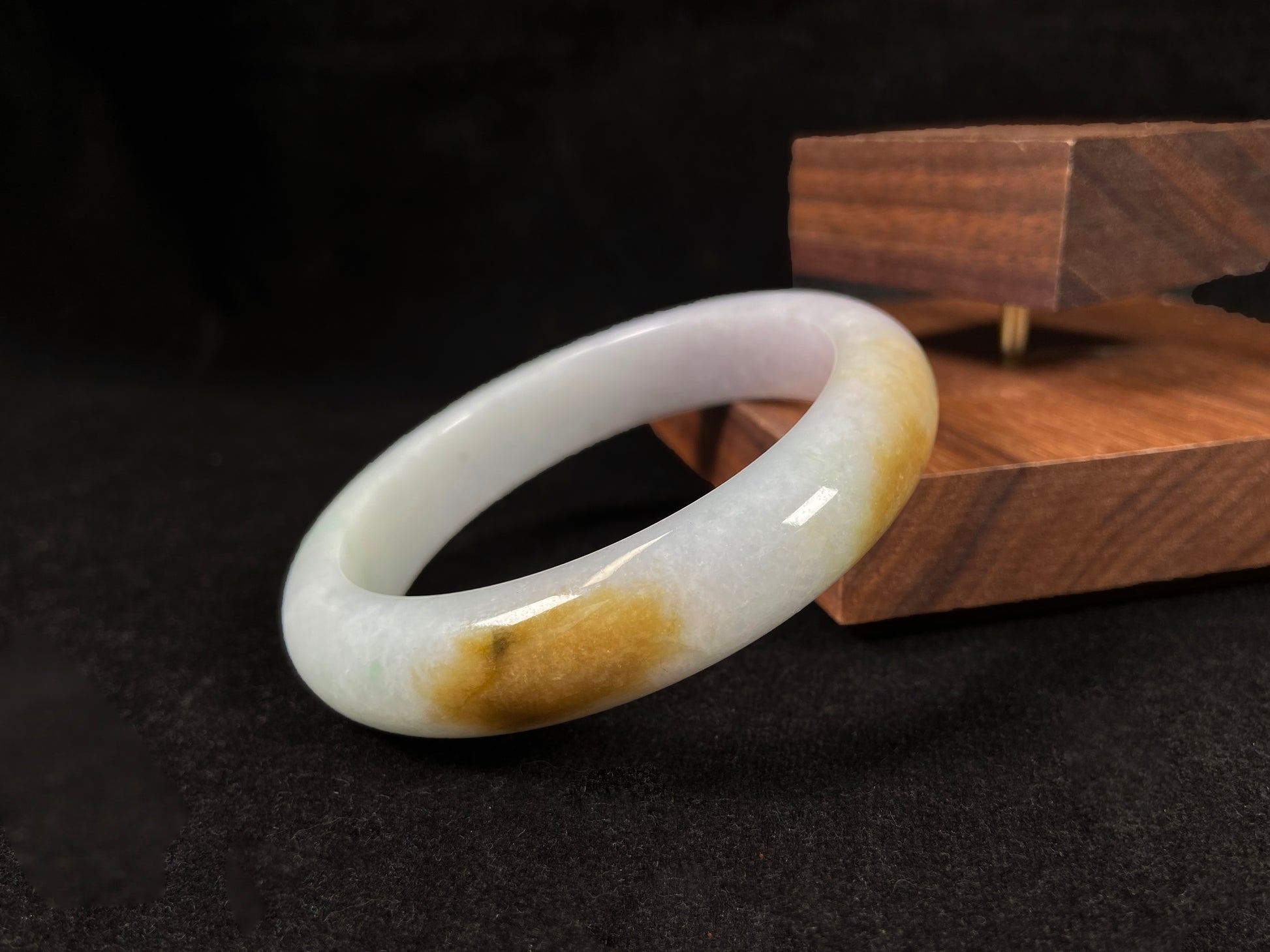 A  white jadeite bangle featuring purple, gold, and light green tones.