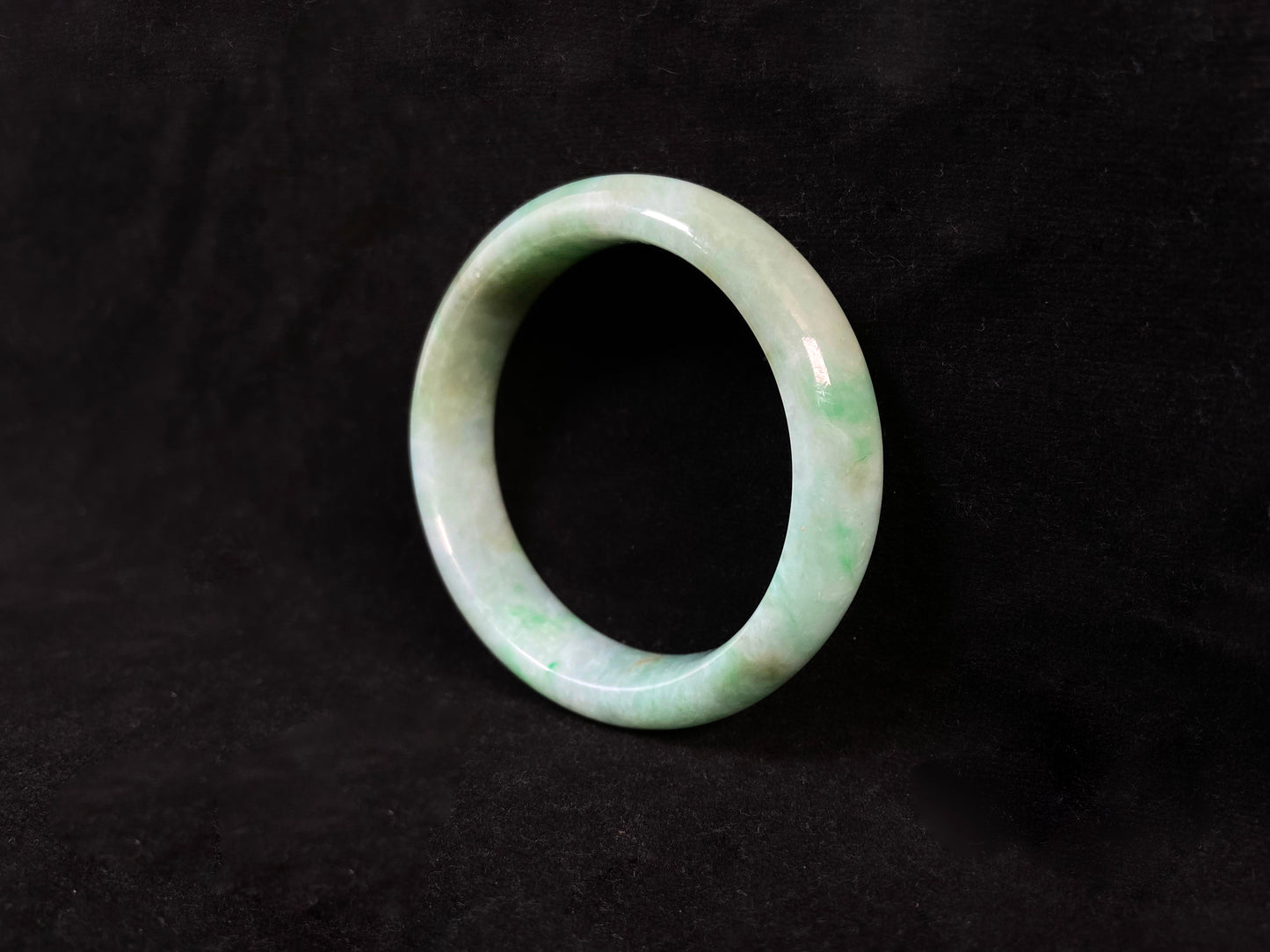 A white-based jade bangle adorned with soft green, deep green and delicate gold speckles.