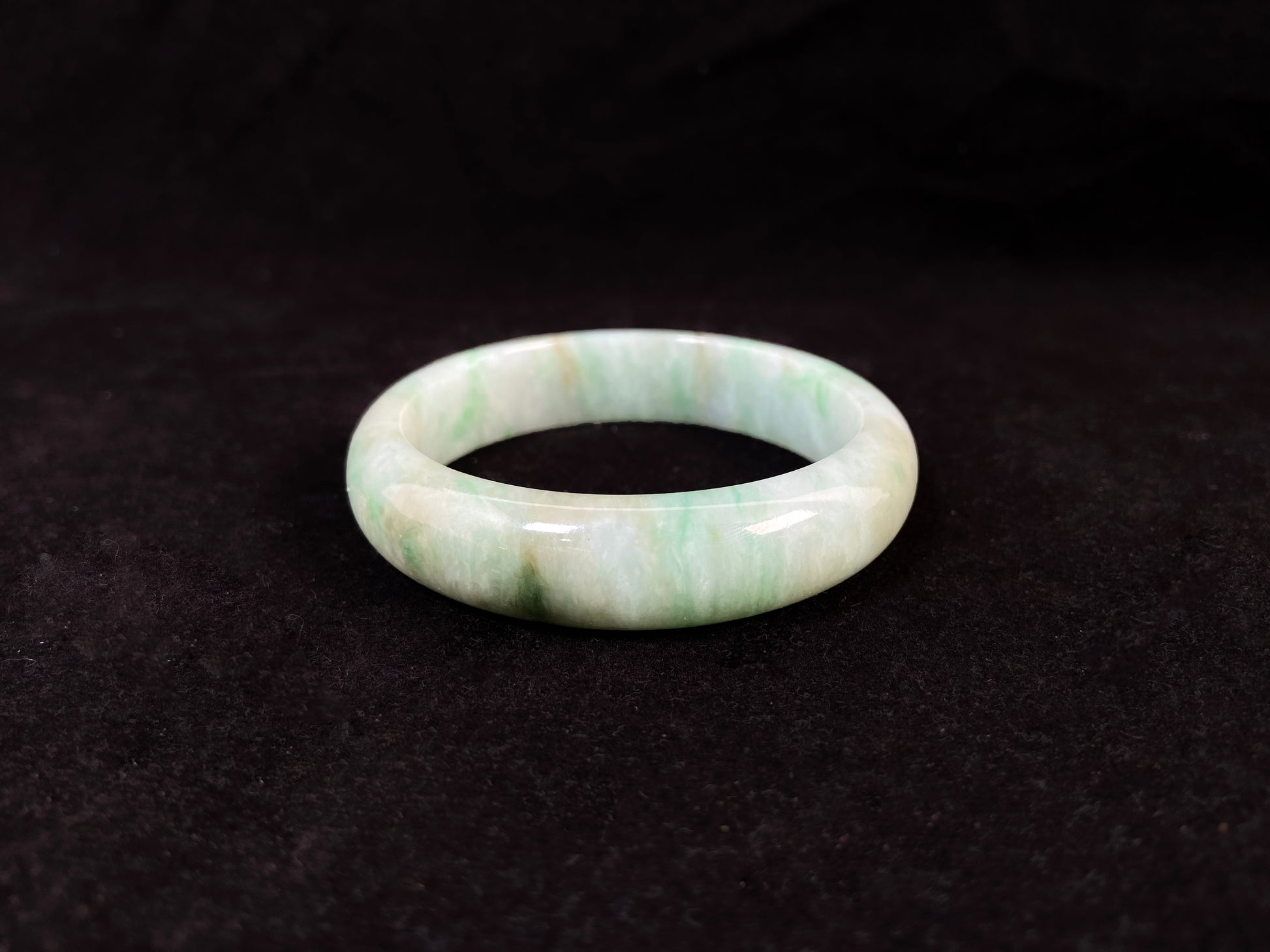 A white-based jade bangle adorned with soft green, deep green patterns and delicate gold speckles.
