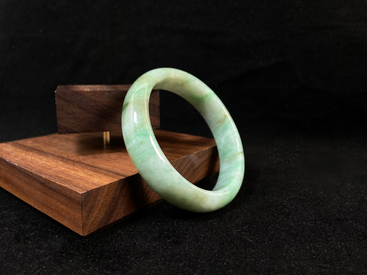 A white-based jade bangle adorned with soft green, deep green and delicate gold speckles.