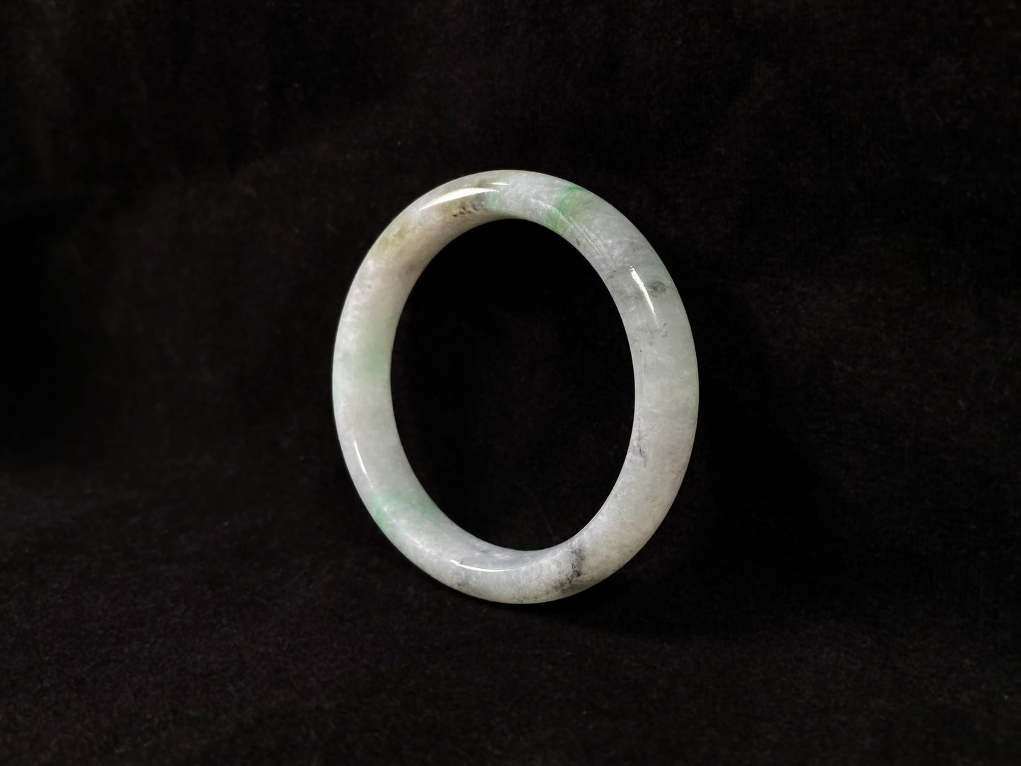 A white jadeite bangle with delicate light green veining and gray speckles.