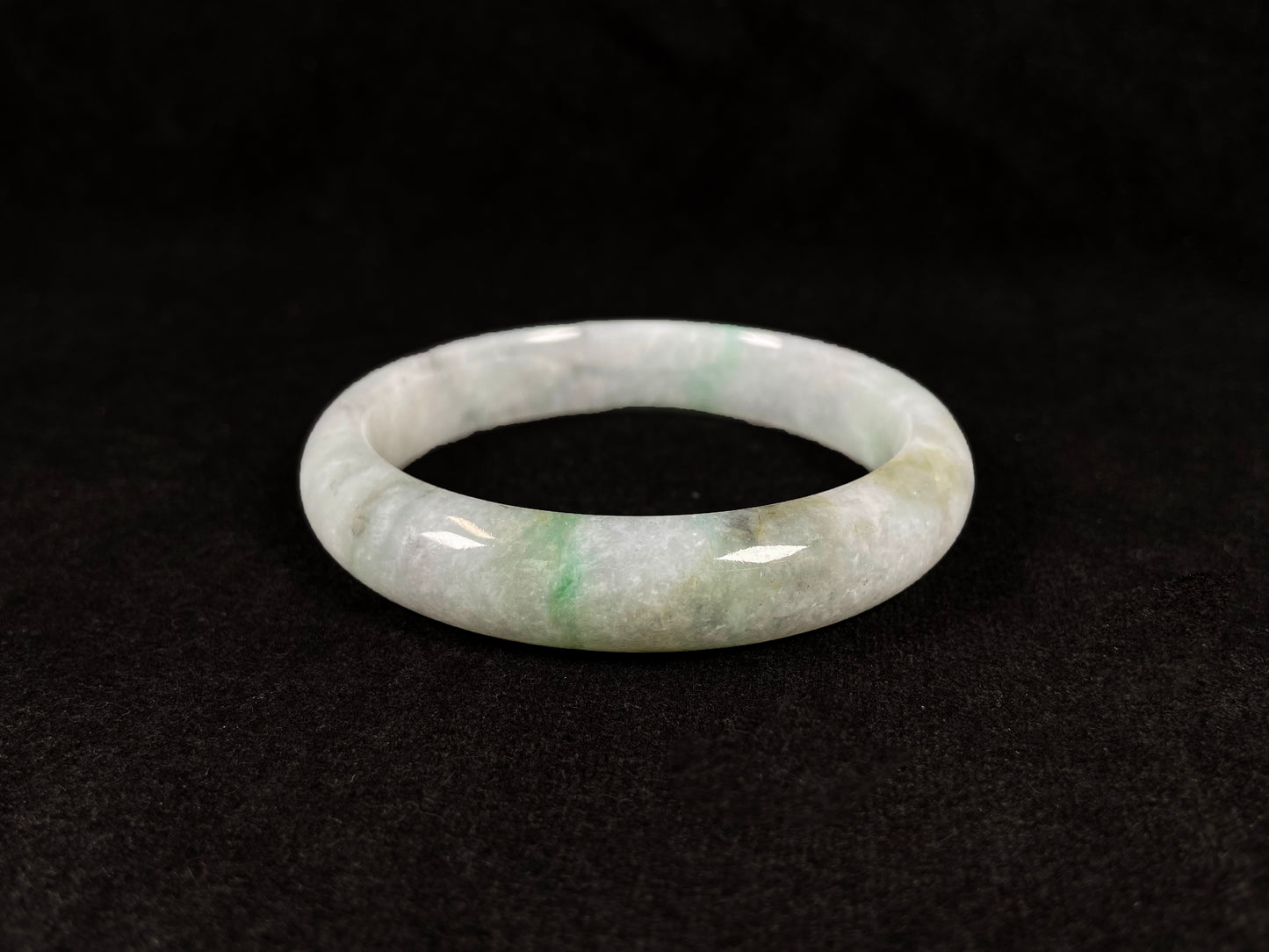 A white jadeite bangle with delicate light green veining and gray speckles.