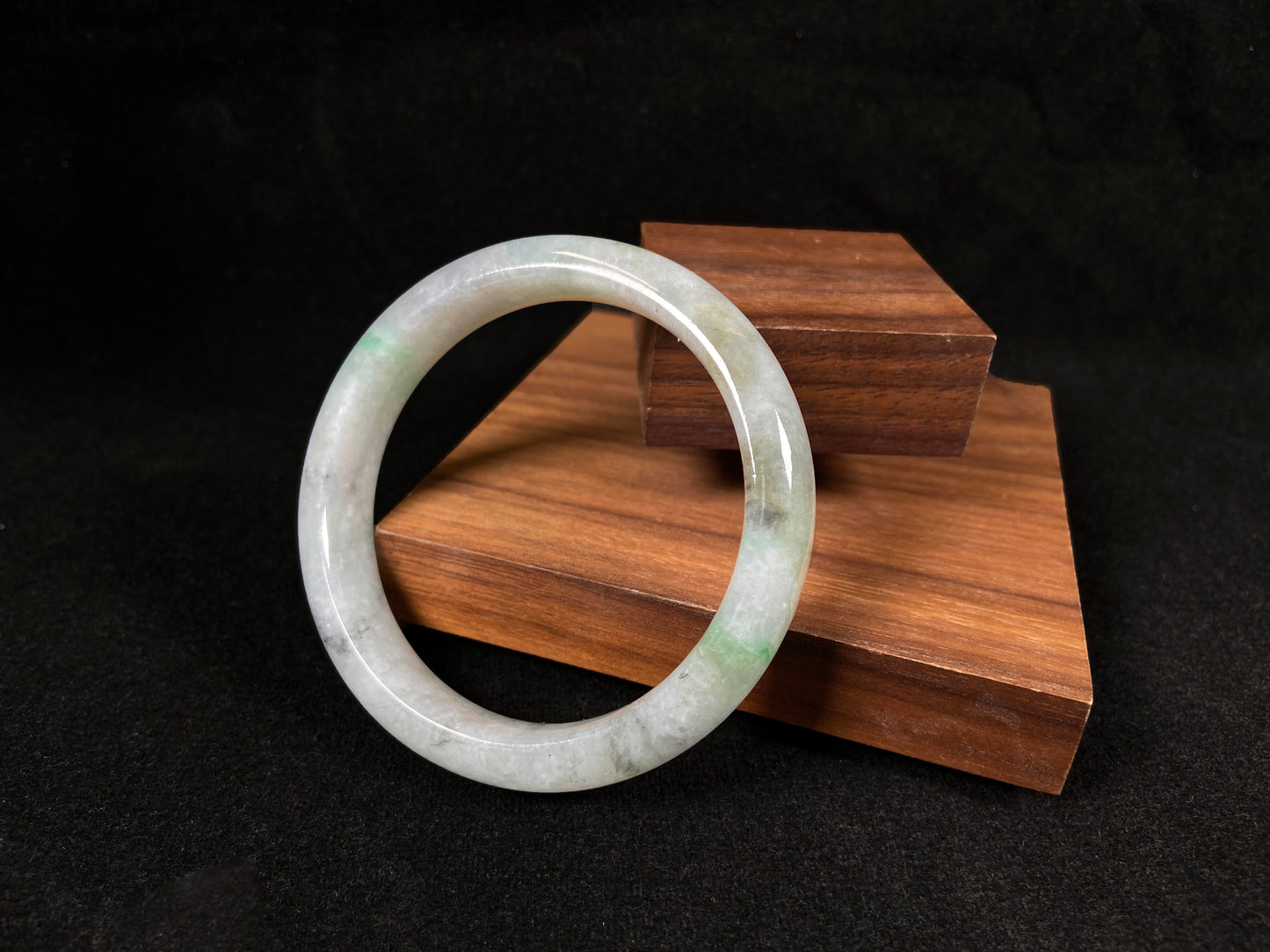 A white jadeite bangle with delicate light green veining and gray speckles.