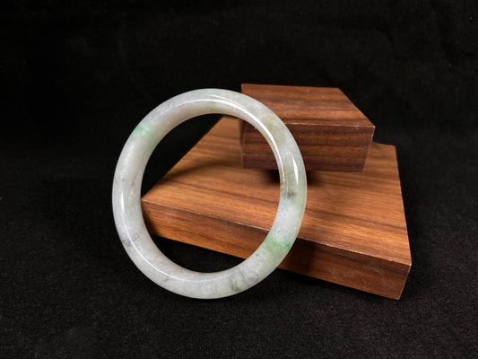 A white jadeite bangle with delicate light green veining and gray speckles.