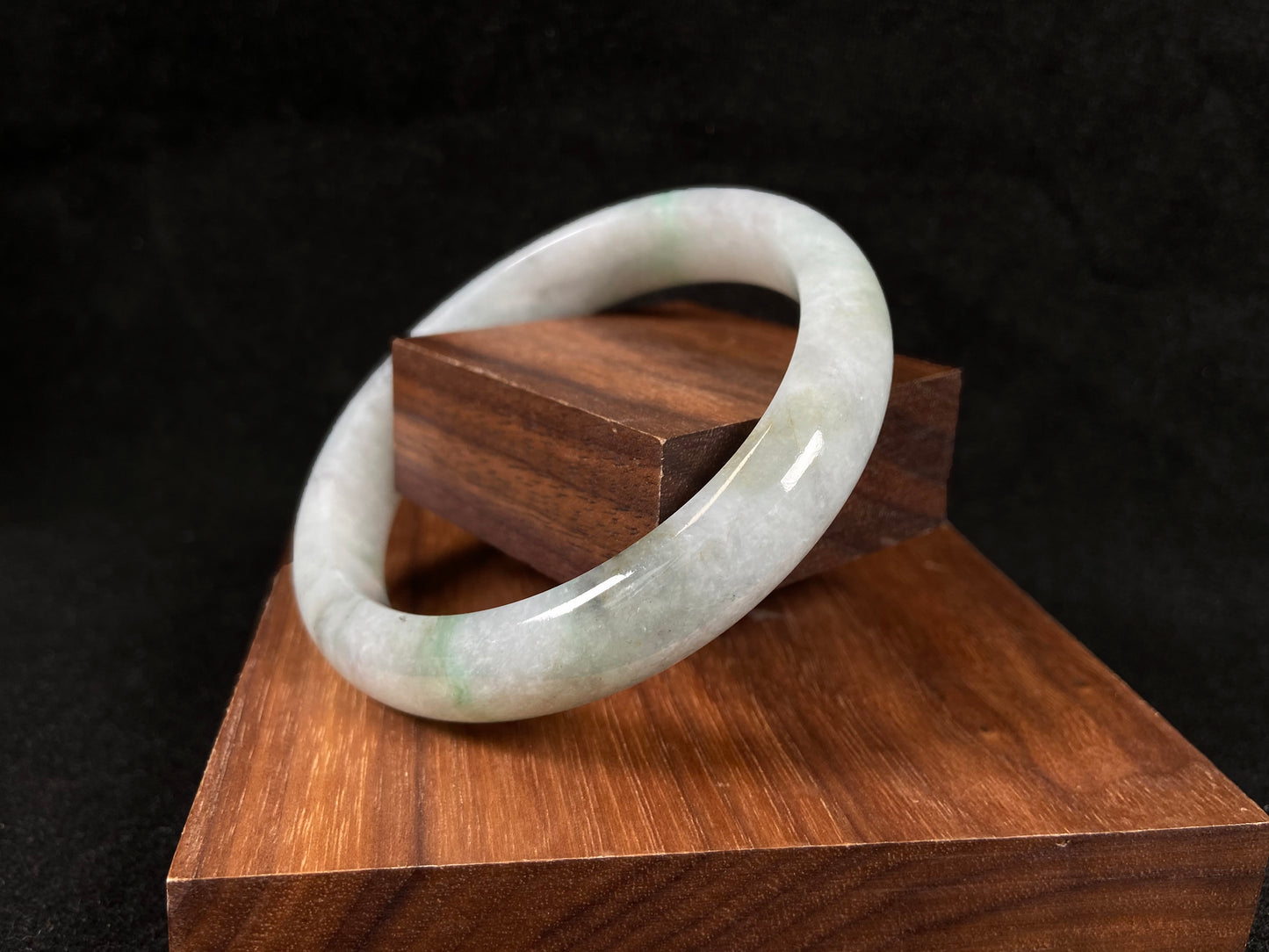 A white jadeite bangle with delicate light green veining and gray speckles.