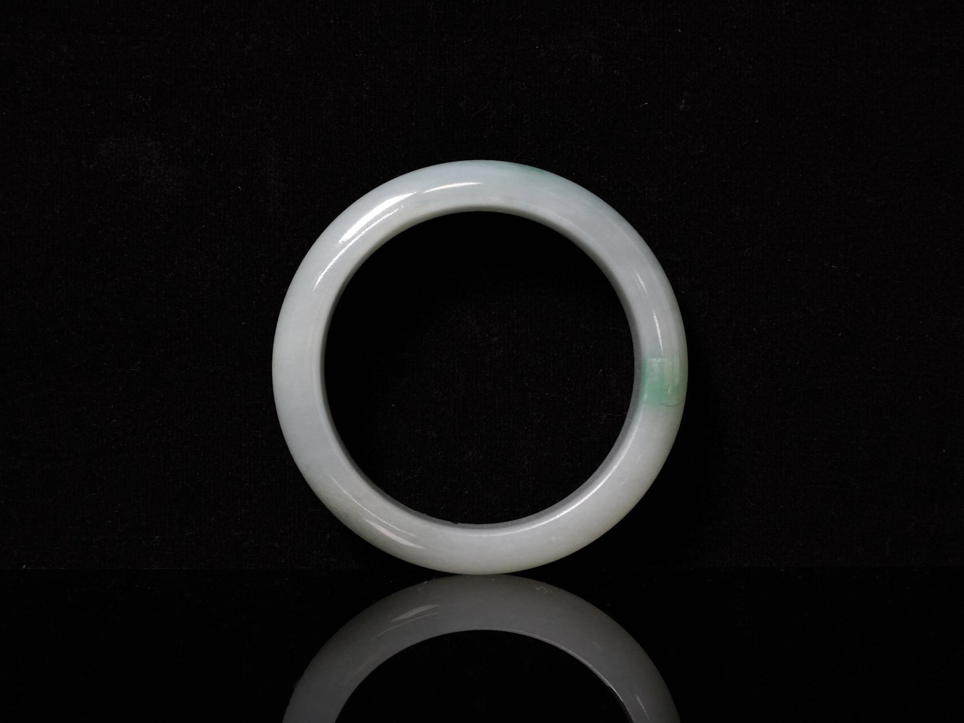 This bangle features a soft, translucent pale white base with a delicate swirl of light emerald green.