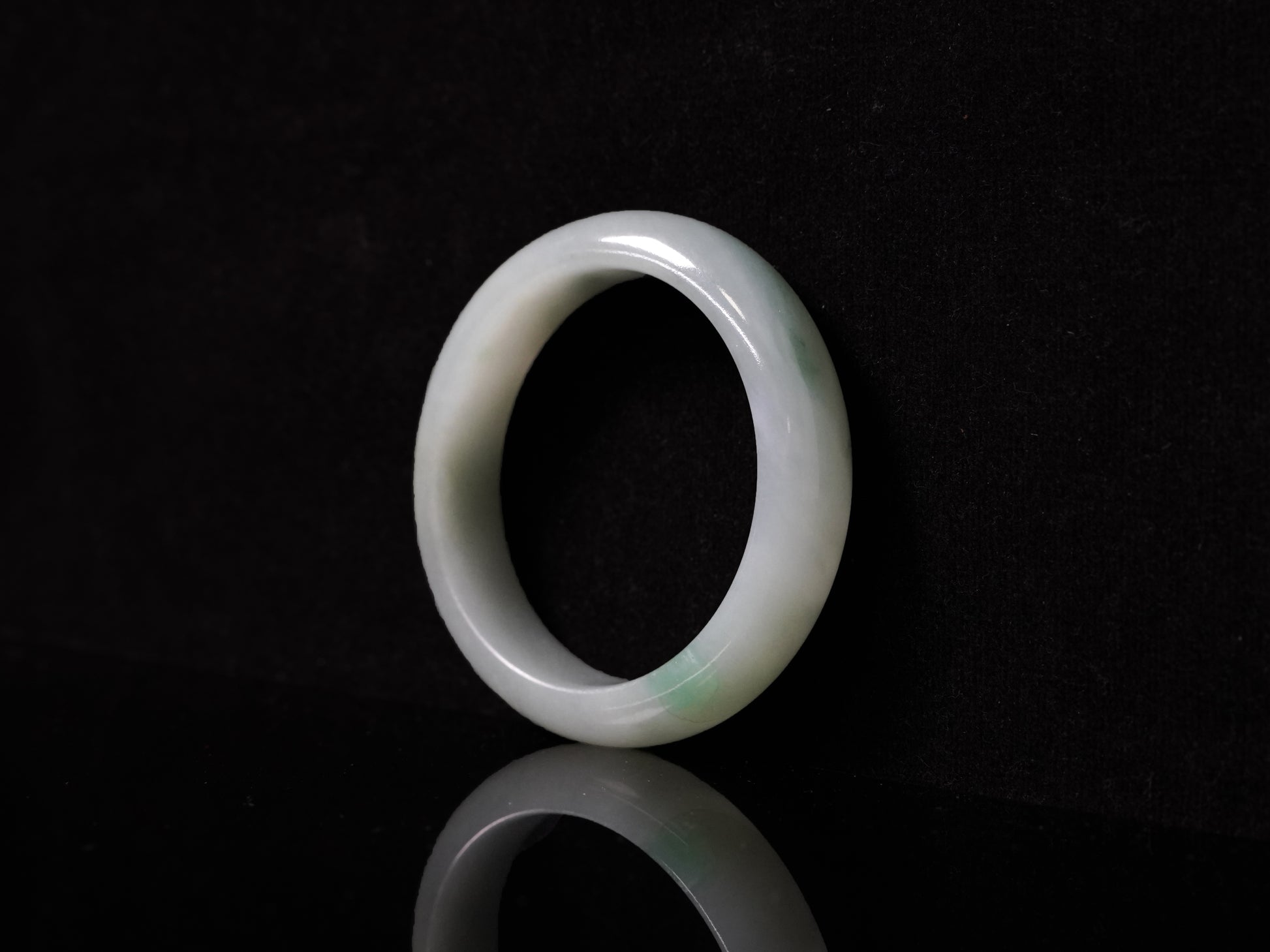 This bangle features a soft, translucent pale white base with a delicate swirl of light emerald green.