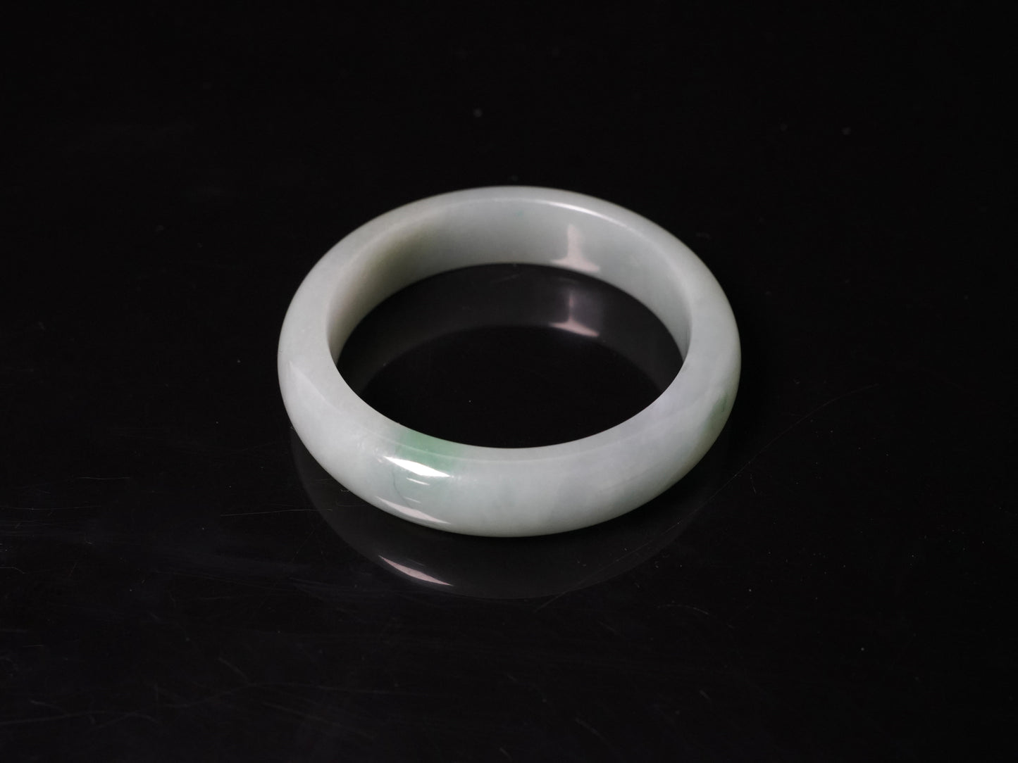 This bangle features a soft, translucent pale white base with a delicate swirl of light emerald green.