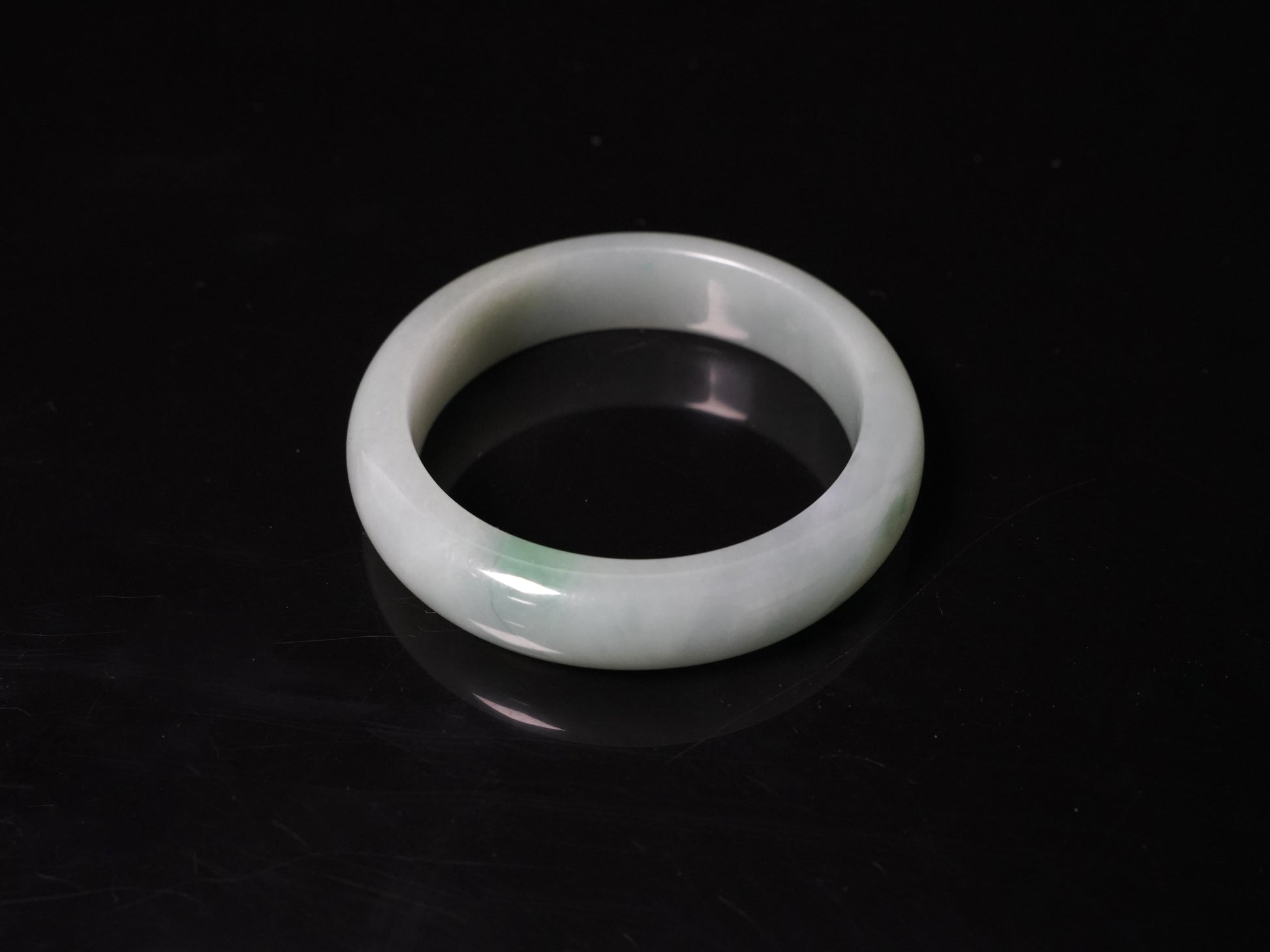 This bangle features a soft, translucent pale white base with a delicate swirl of light emerald green.
