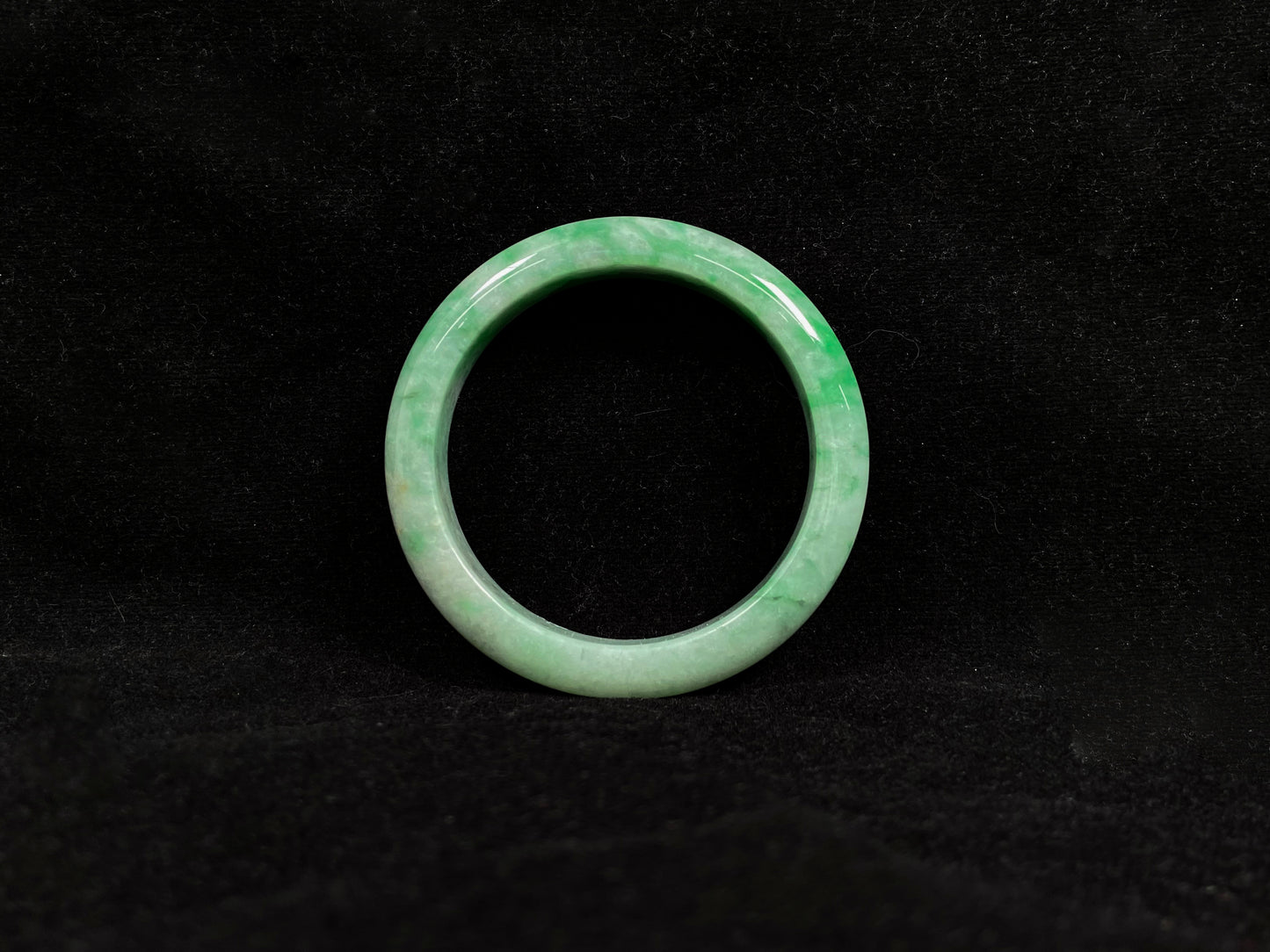 This white-based jade bangle features evenly distributed vibrant green.