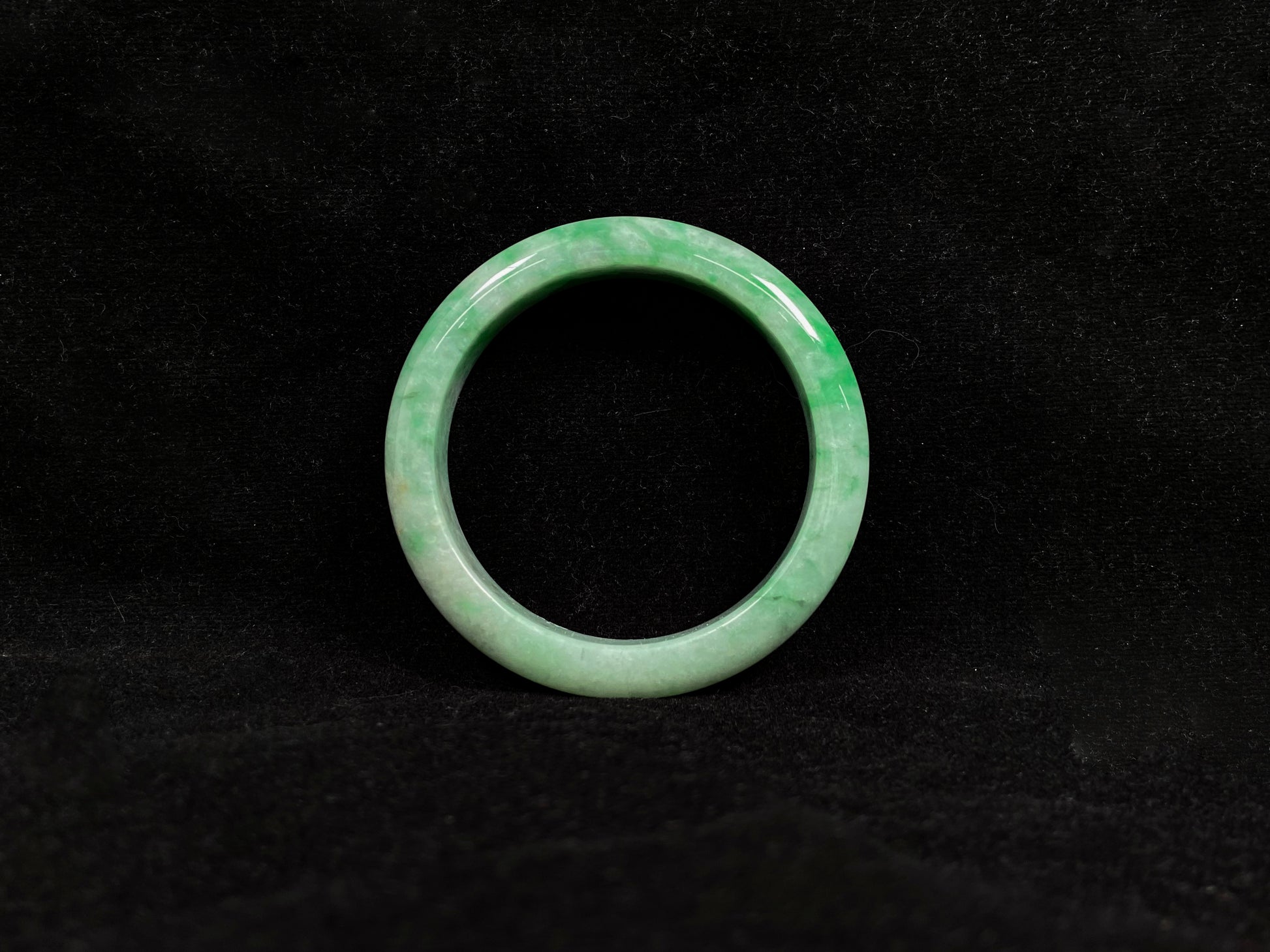 This white-based jade bangle features evenly distributed vibrant green.