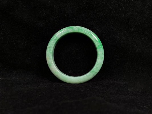 This white-based jade bangle features evenly distributed vibrant green.