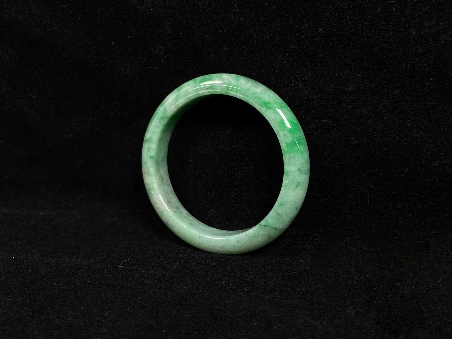 This white-based jade bangle features evenly distributed vibrant green.