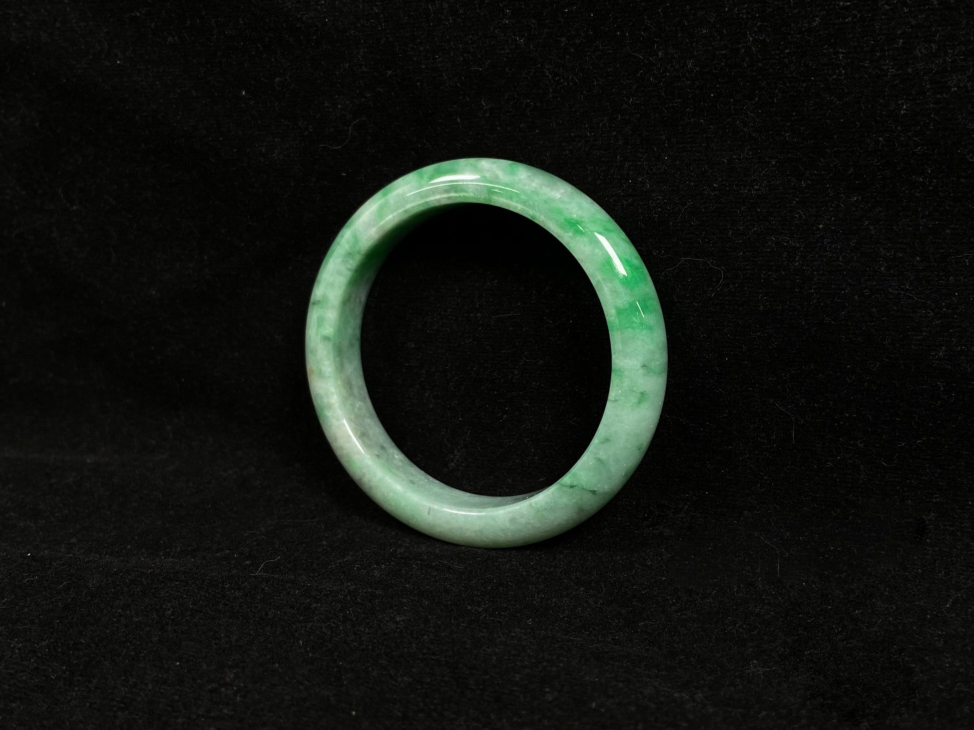 This white-based jade bangle features evenly distributed vibrant green.