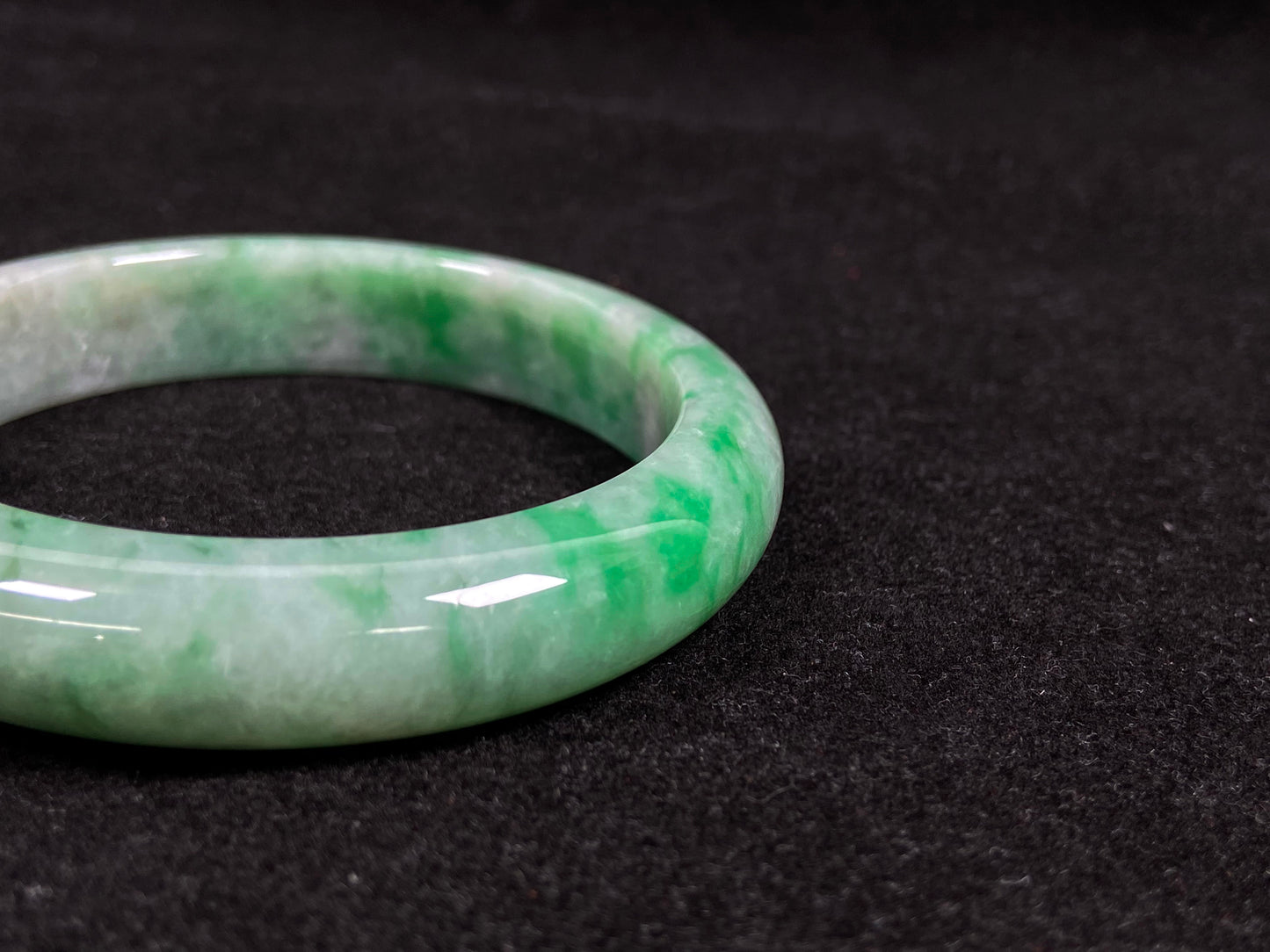 This white-based jade bangle features evenly distributed vibrant green.
