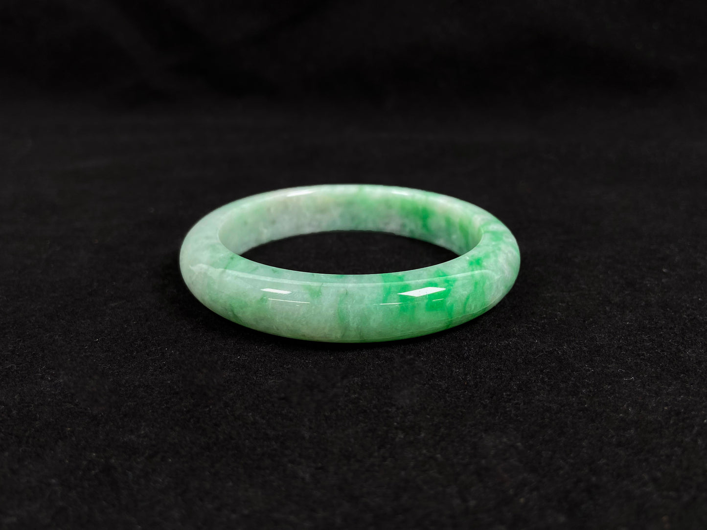 This white-based jade bangle features evenly distributed vibrant green.