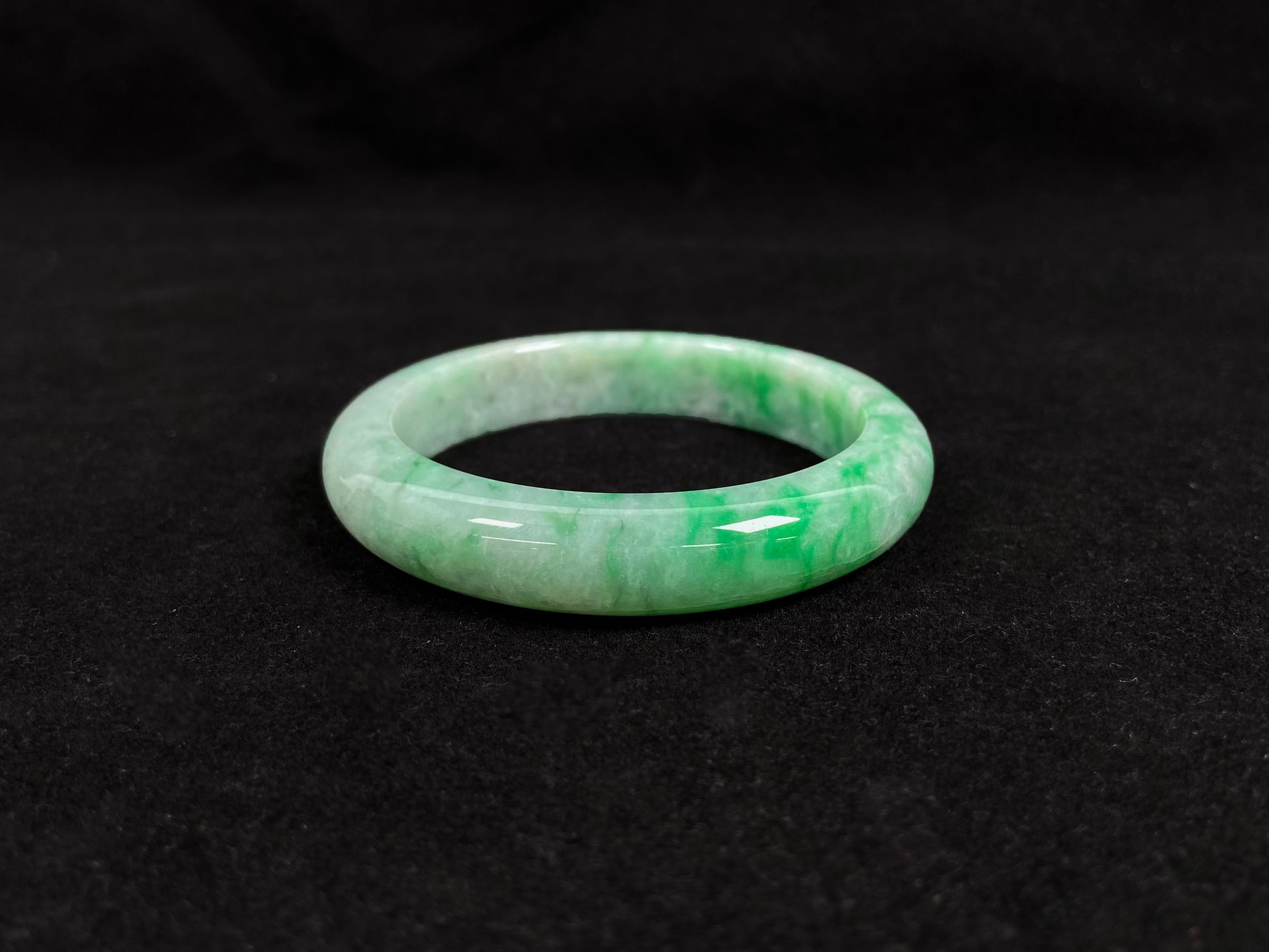 This white-based jade bangle features evenly distributed vibrant green.