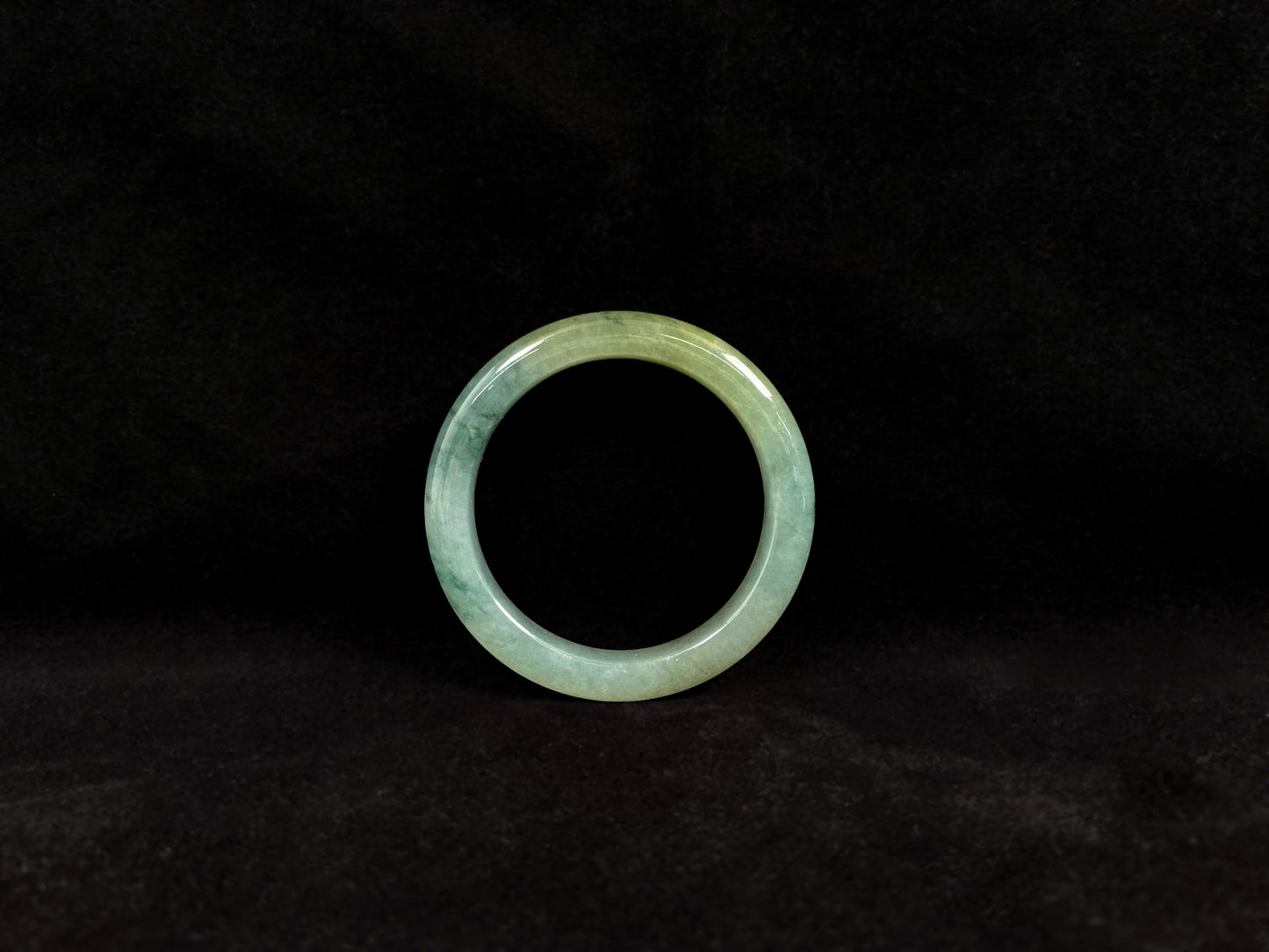 This jadeite bangle features a light green translucent base with floating green patches and integral areas of golden.