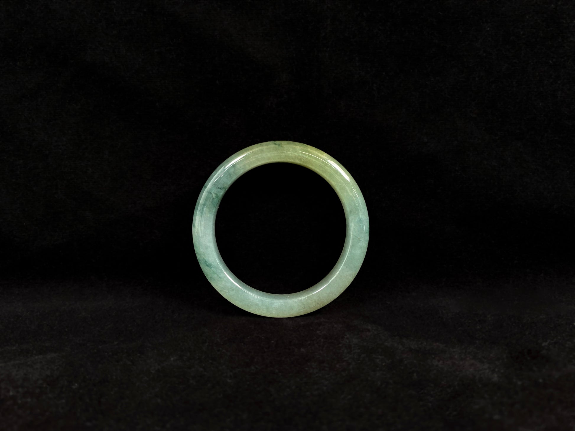 This jadeite bangle features a light green translucent base with floating green patches and integral areas of golden.