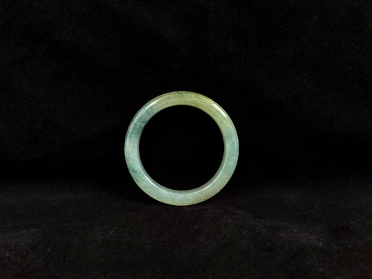This jadeite bangle features a light green translucent base with floating green patches and integral areas of golden.
