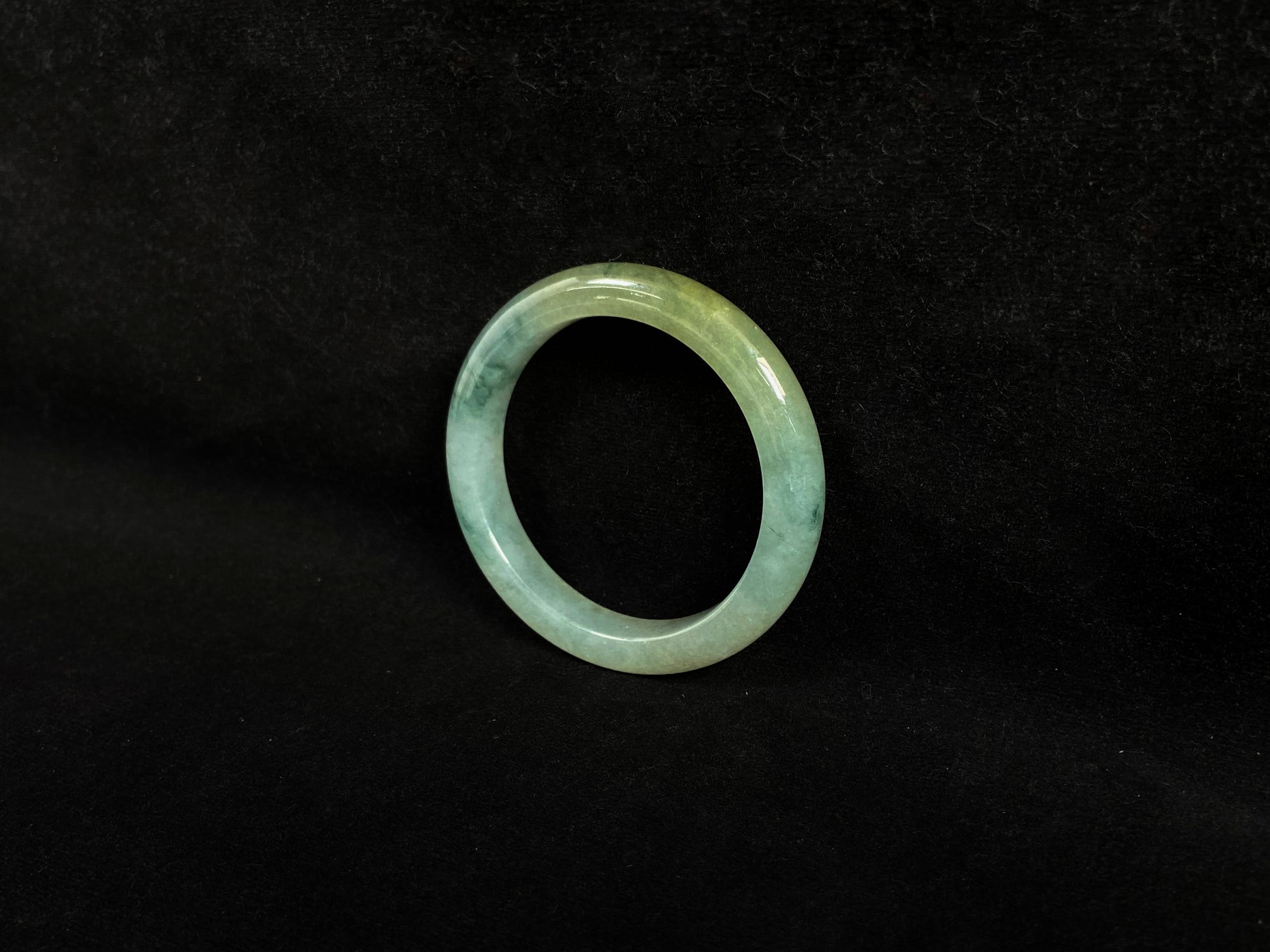 This jadeite bangle features a light green translucent base with floating green patches and integral areas of golden.