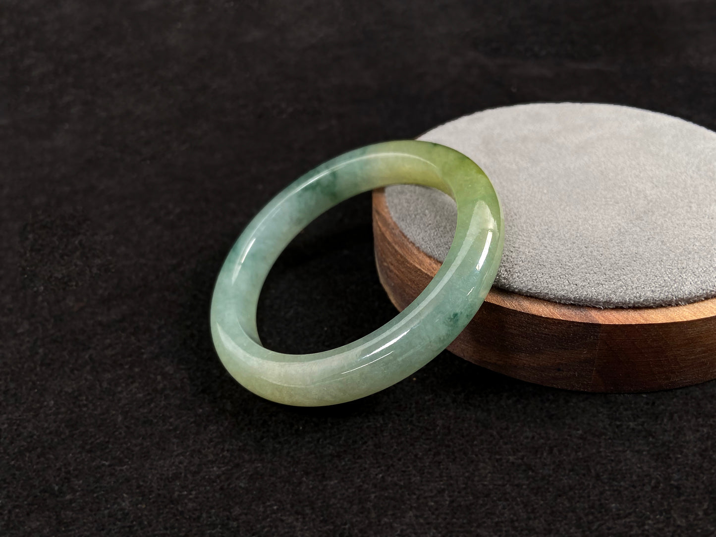 This jadeite bangle features a light green translucent base with floating green patches and integral areas of golden.