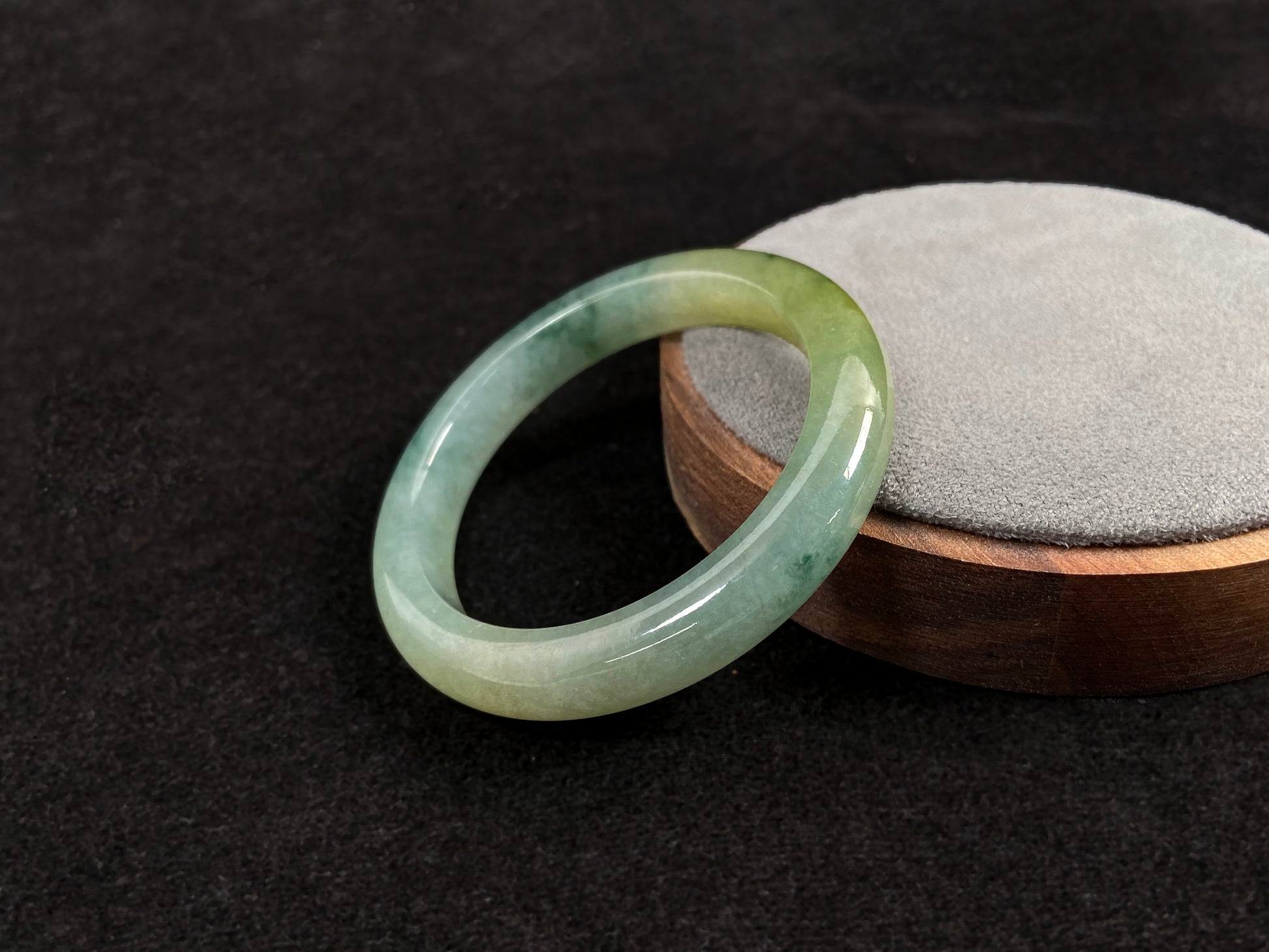 This jadeite bangle features a light green translucent base with floating green patches and integral areas of golden.