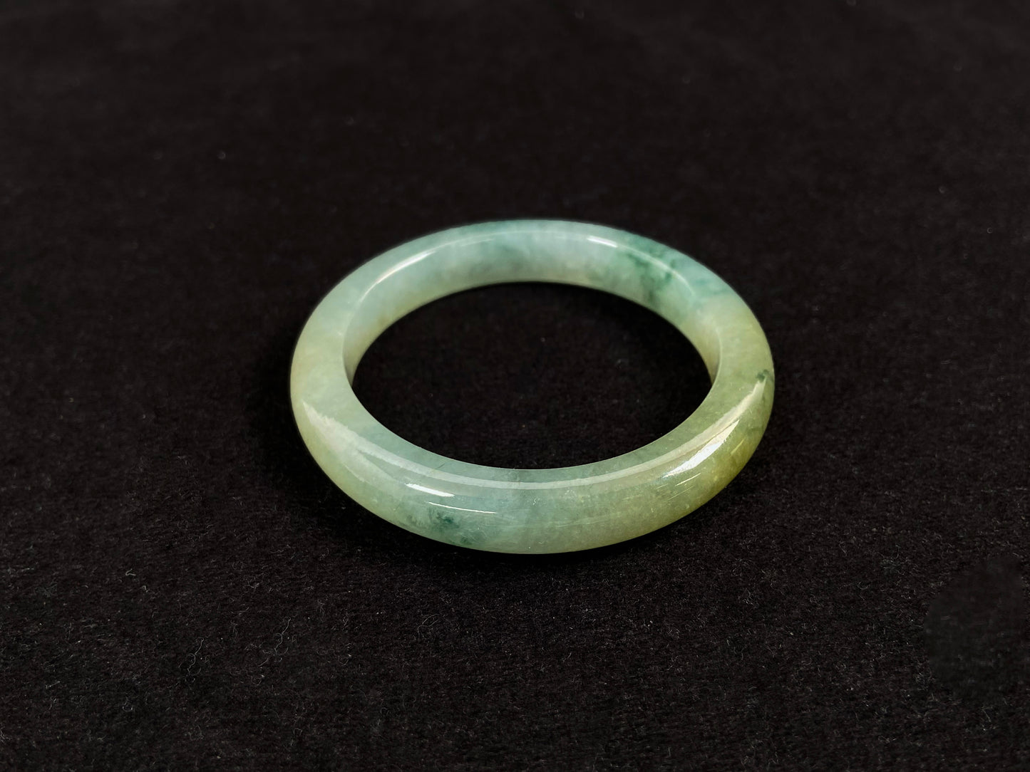 This jadeite bangle features a light green translucent base with floating green patches and integral areas of golden.