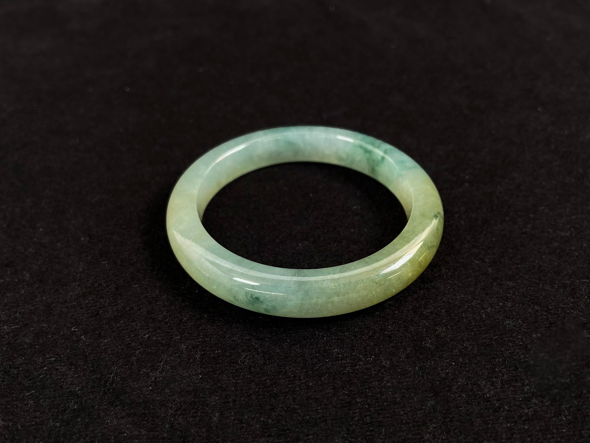This jadeite bangle features a light green translucent base with floating green patches and integral areas of golden.