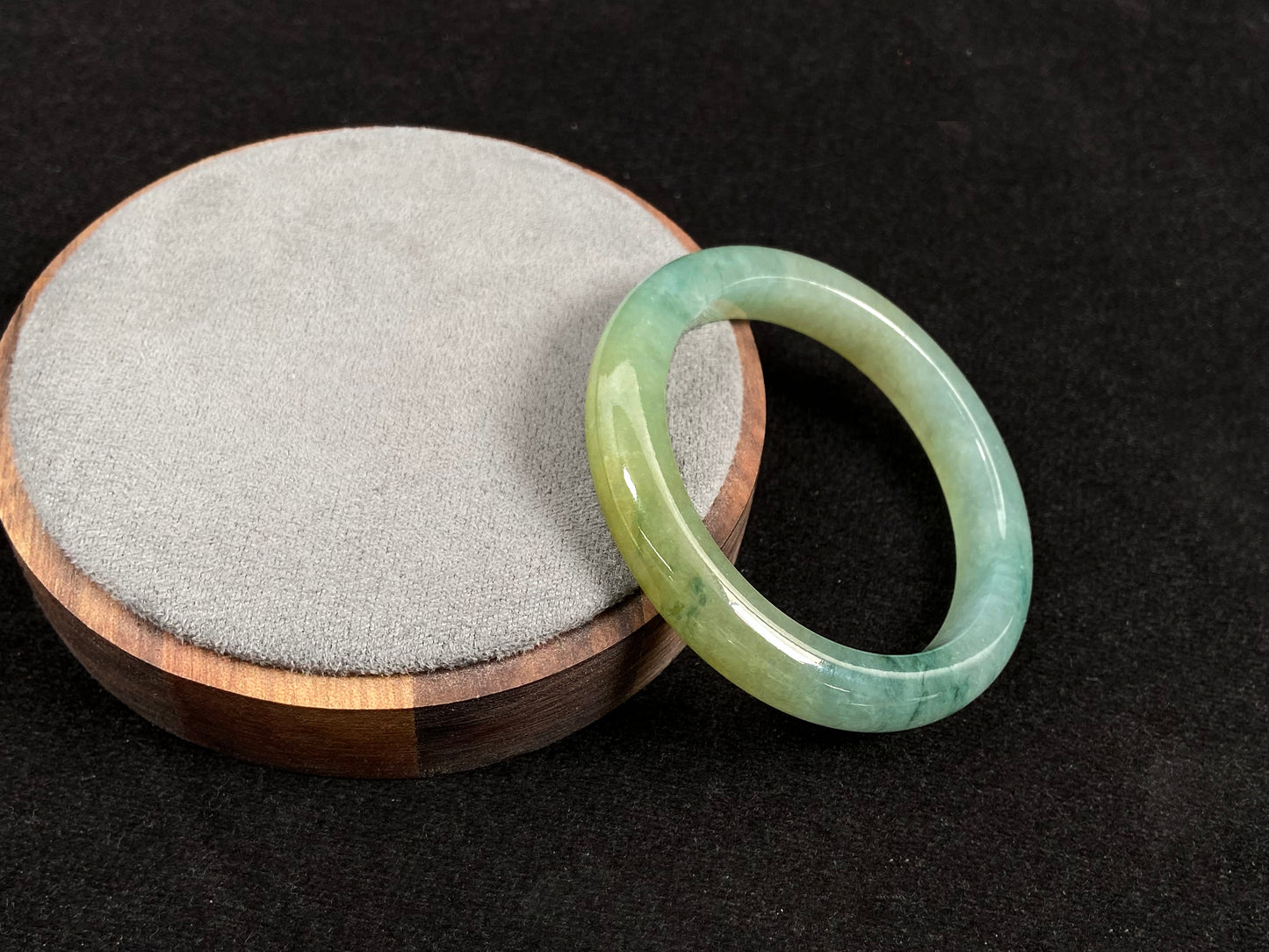 This jadeite bangle features a light green translucent base with floating green patches and integral areas of golden.